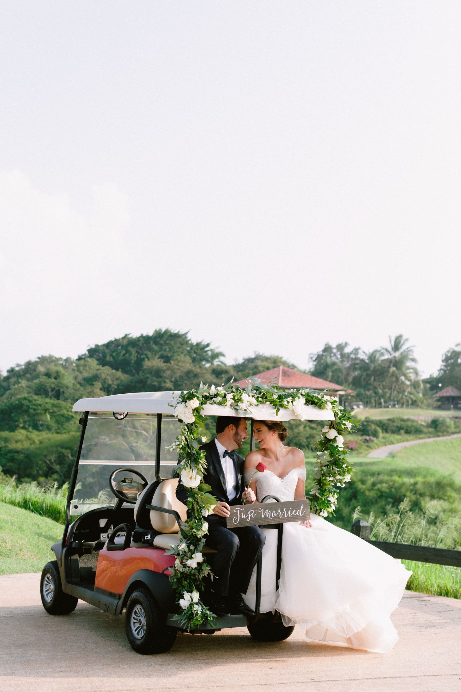 Wedding couple riding in a decorated golf cart on a lush green course.
