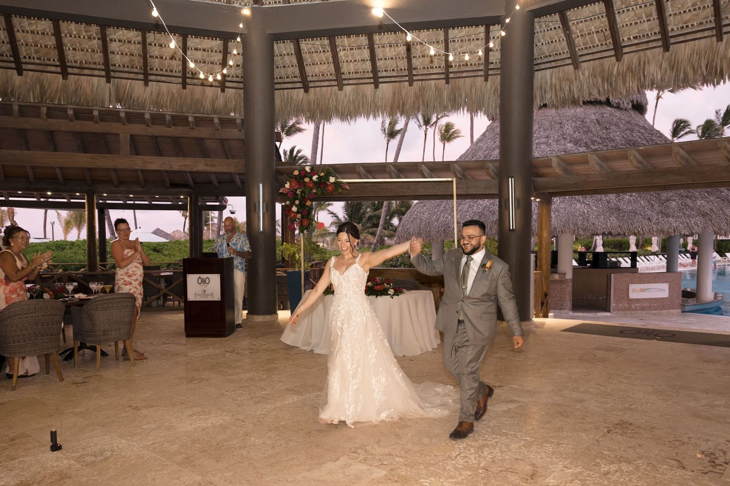 A panoramic view of a rustic open-air pavilion with thatched roof and wooden beams in a tropical setting.