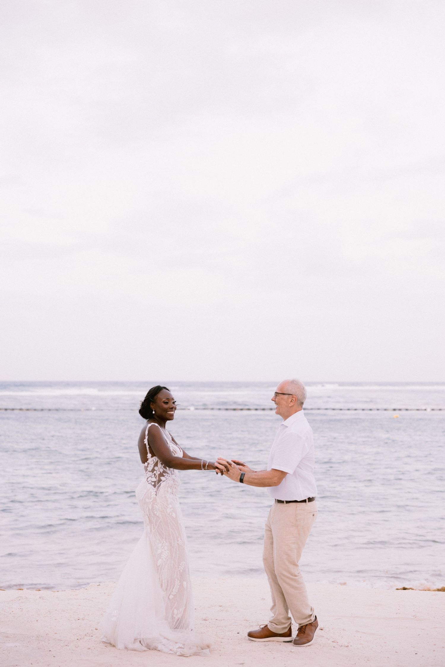 A couple in wedding attire holds hands and shares a romantic moment on a beach at sunset.