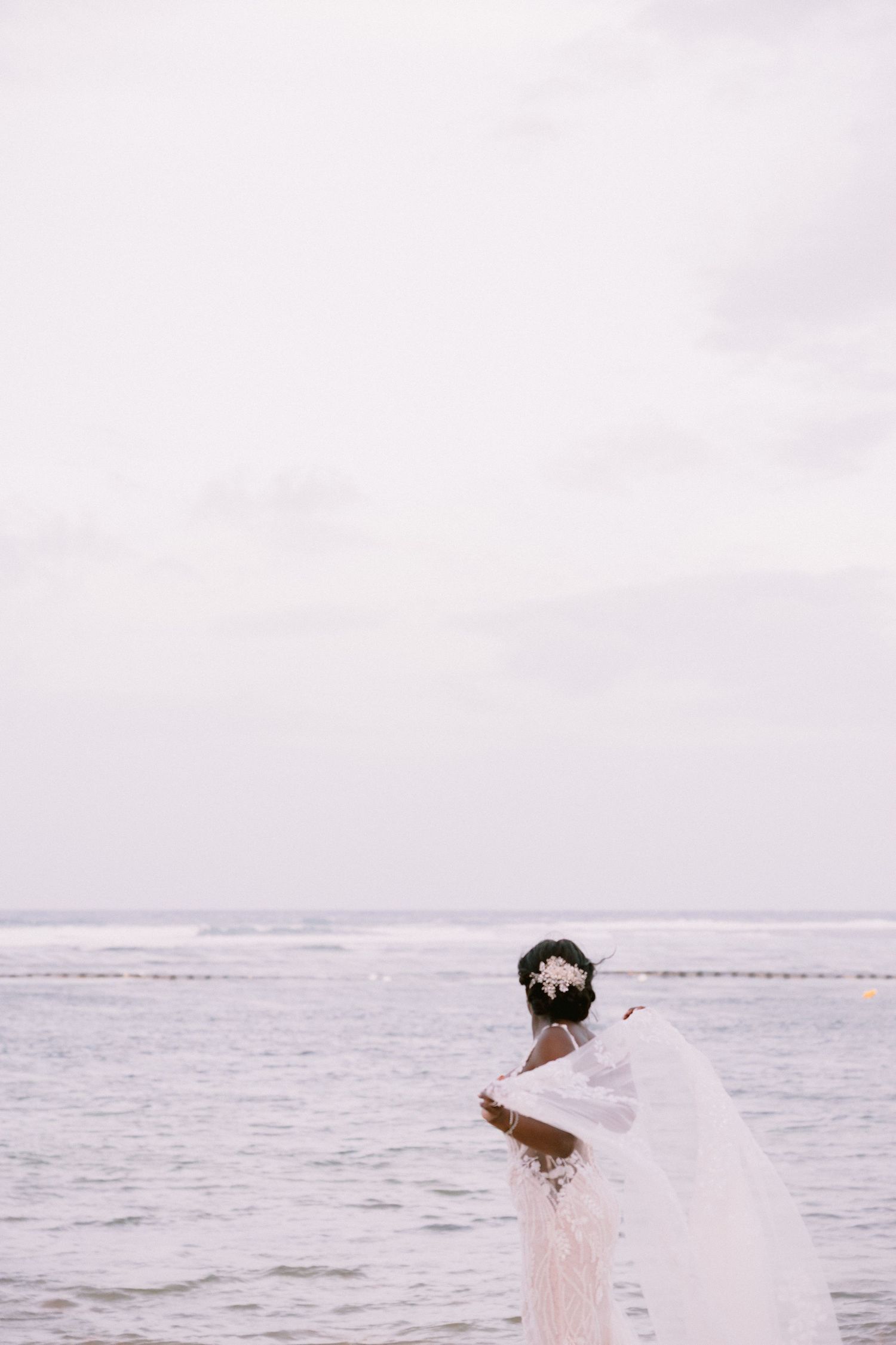 A couple in wedding attire embraces on a misty beach with the ocean waves in the background.