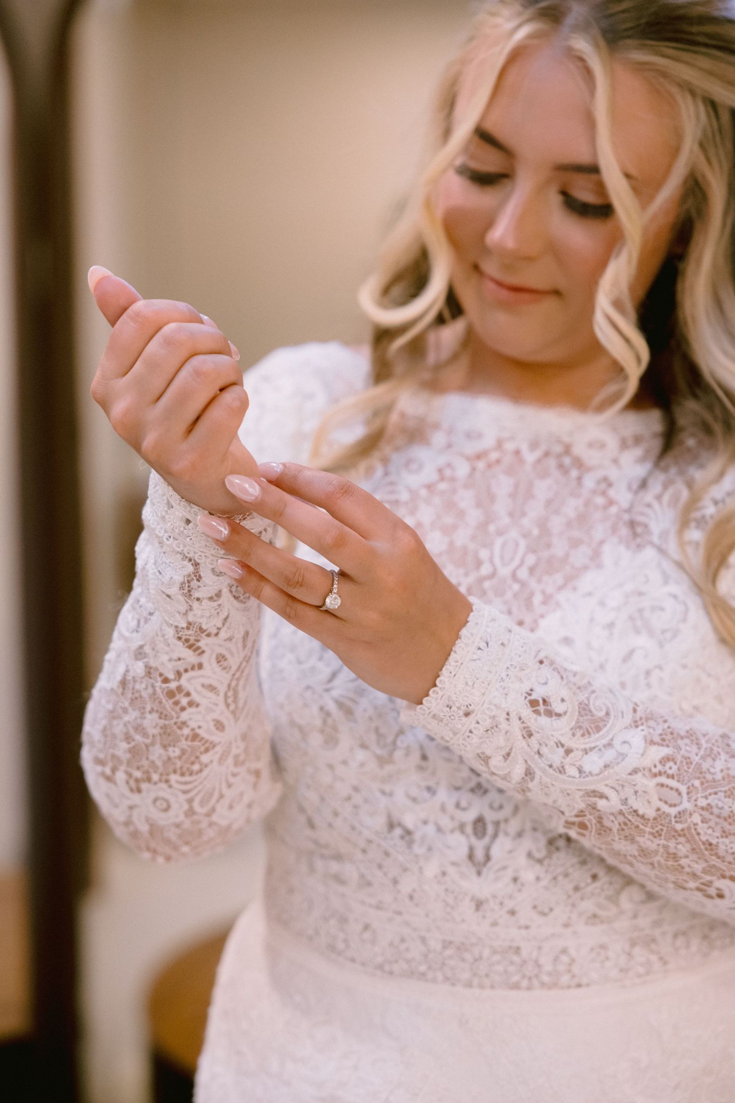 Bride in long-sleeve lace wedding dress admiring her engagement ring while getting ready.