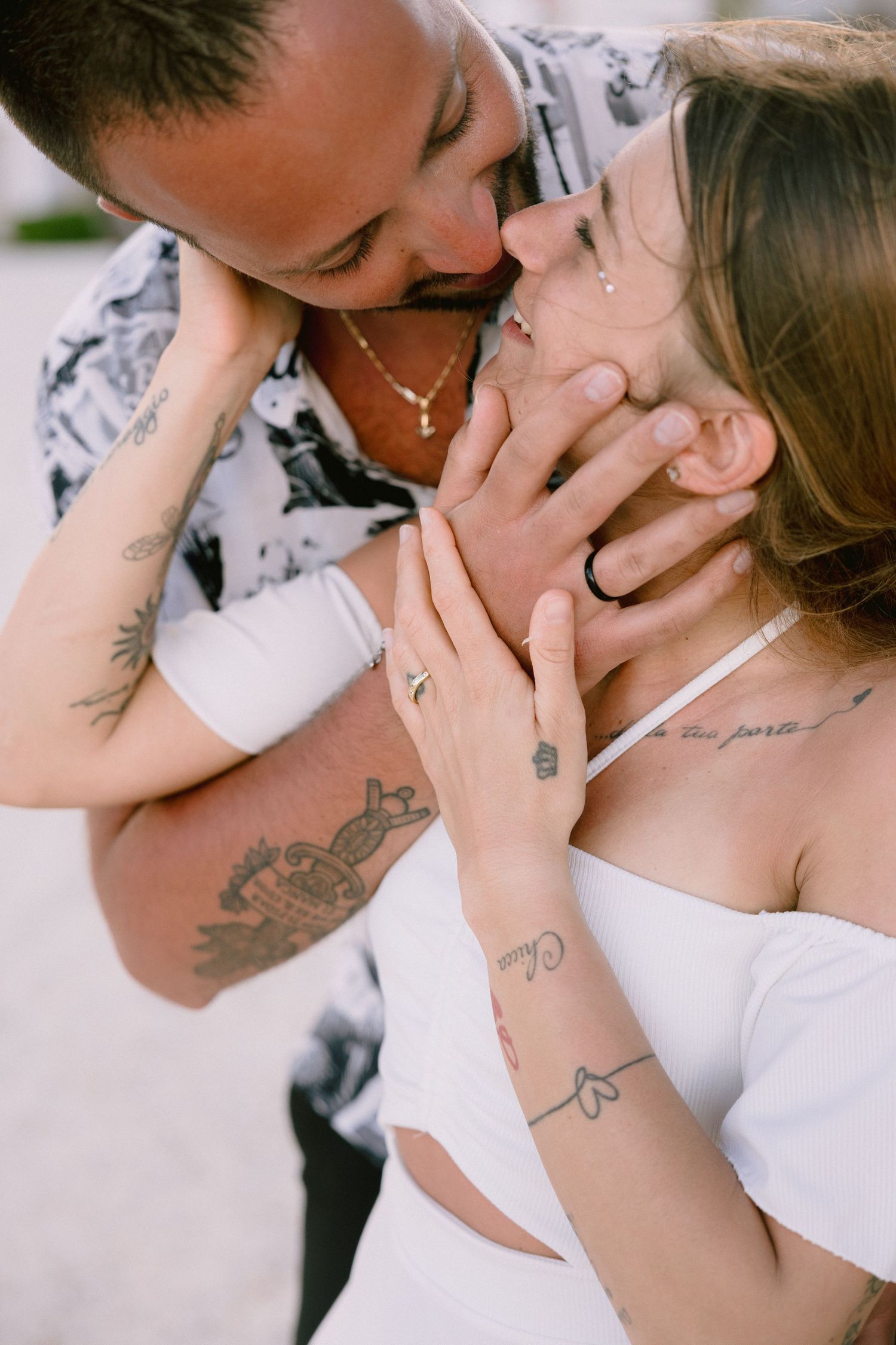 Tattooed couple sharing an intimate moment, man gently holding woman's face for a kiss outdoors.
