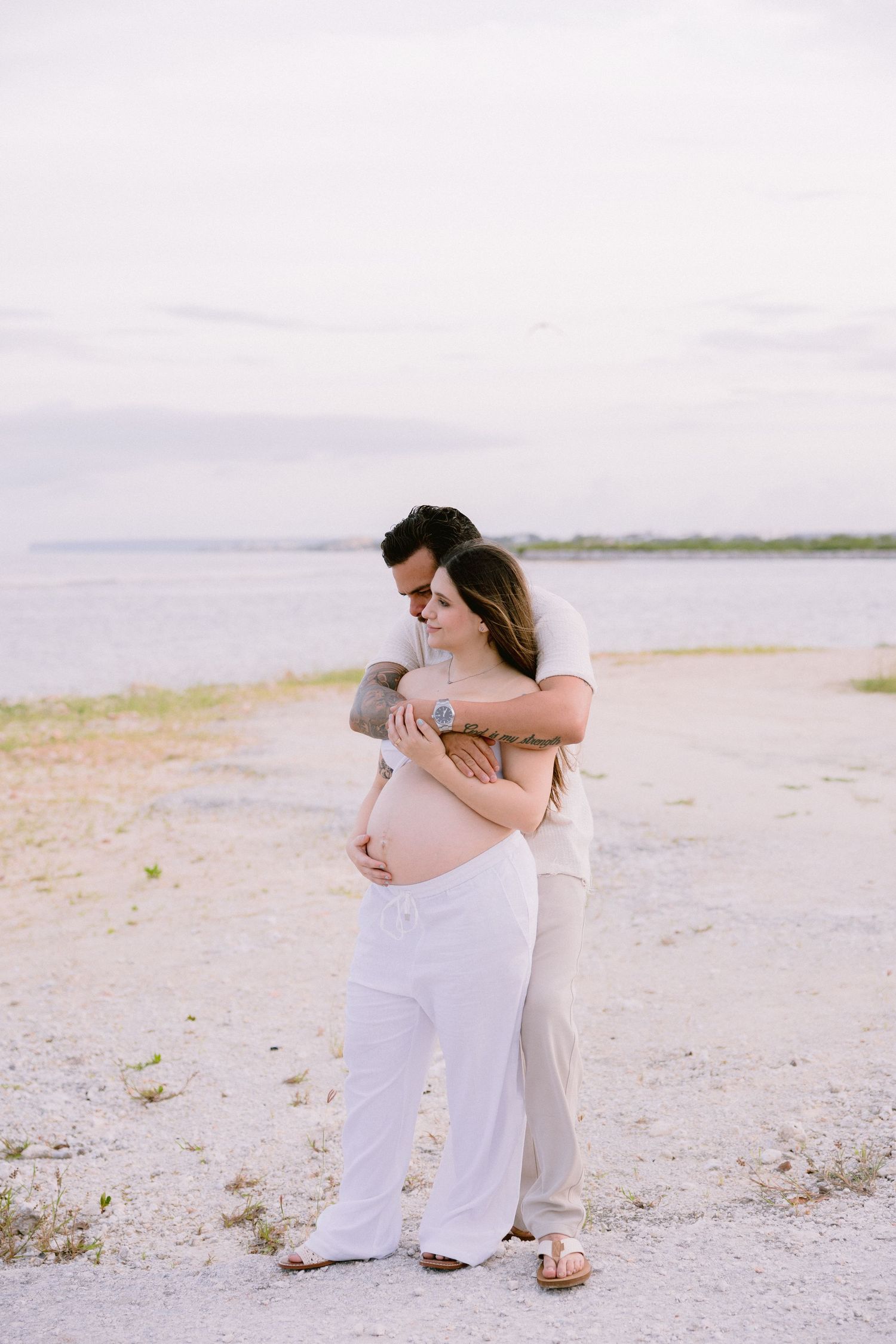 A tender beachside embrace captured in soft pastel tones as couple shares an intimate moment on sandy shore.