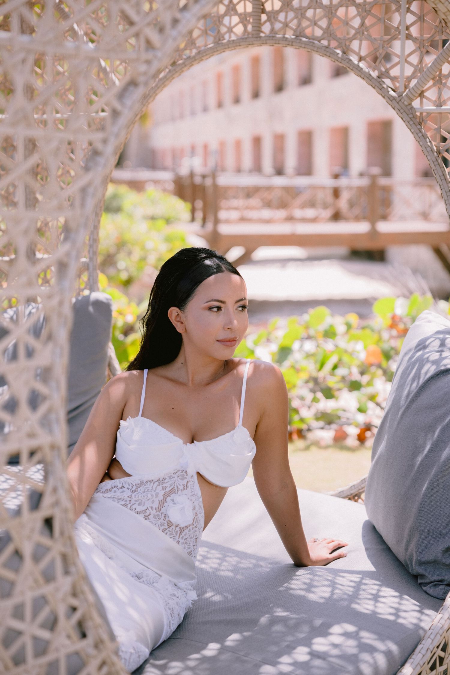 A woman in a white lace dress relaxes in a wicker cabana chair at a punta cana luxury resort outdoor lounge