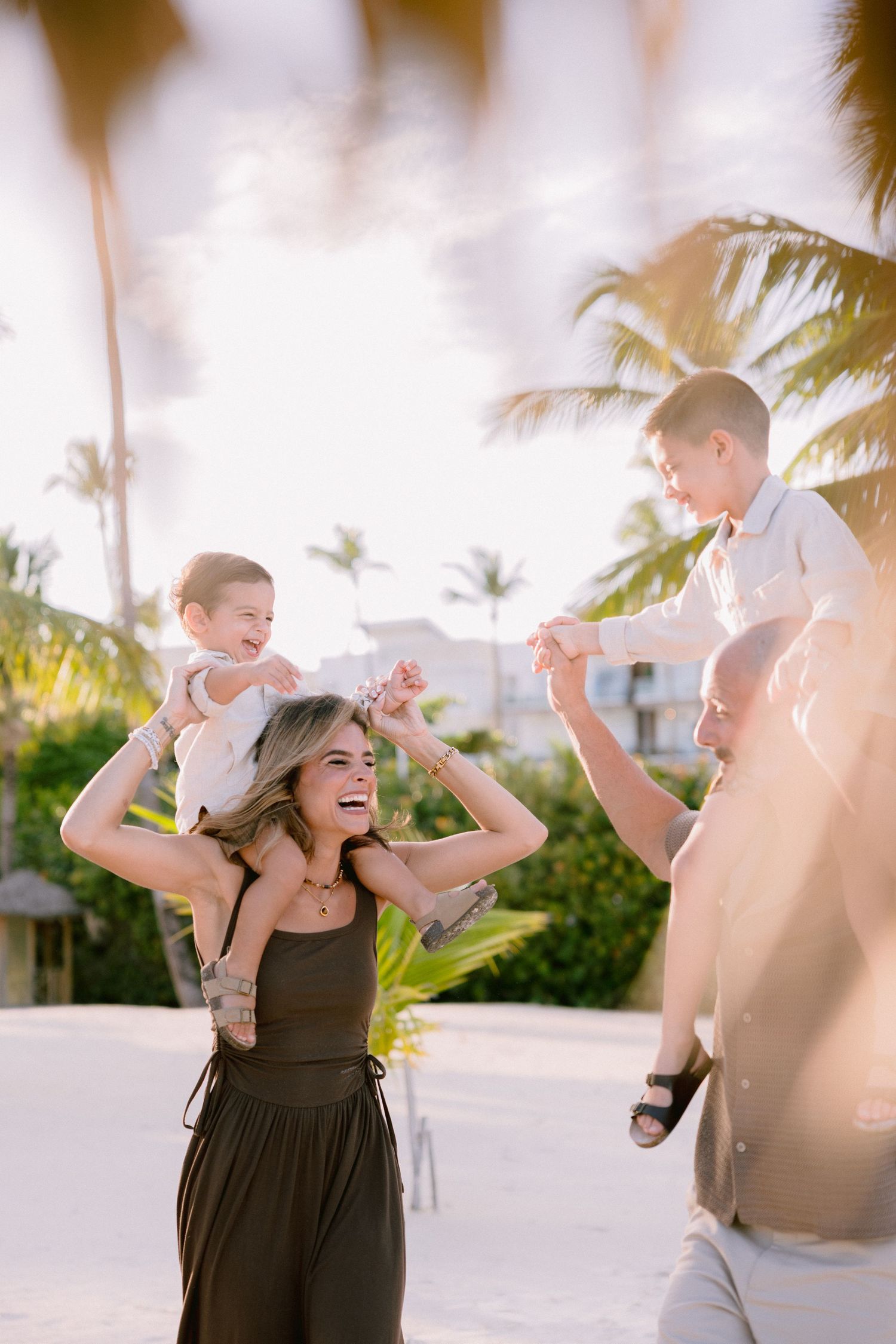 A parent and child share joyful moments together while playing on a sunny beach with palm trees in the background.