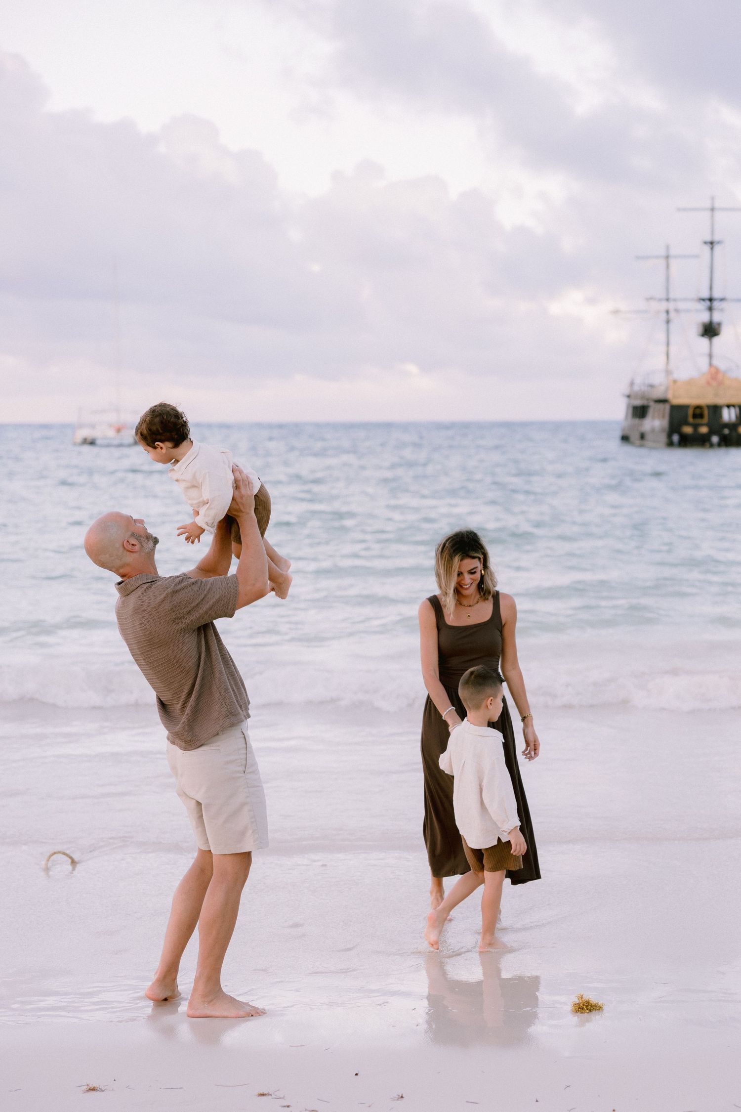 Family plays together in shallow ocean water at sunset on a tropical beach, creating playful moments in sequence.