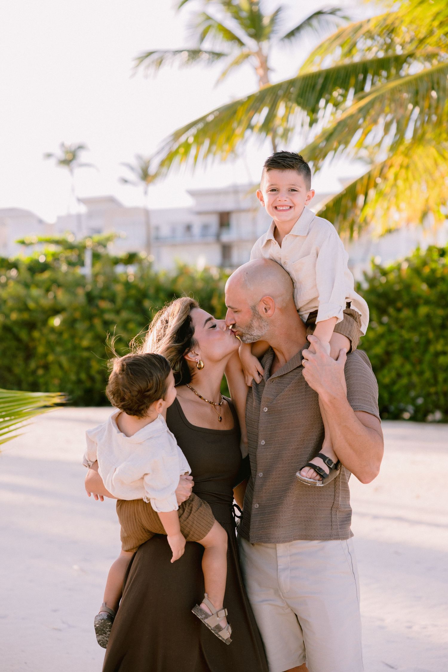 A loving family shares a tender moment together under a palm tree in a tropical setting during golden hour.