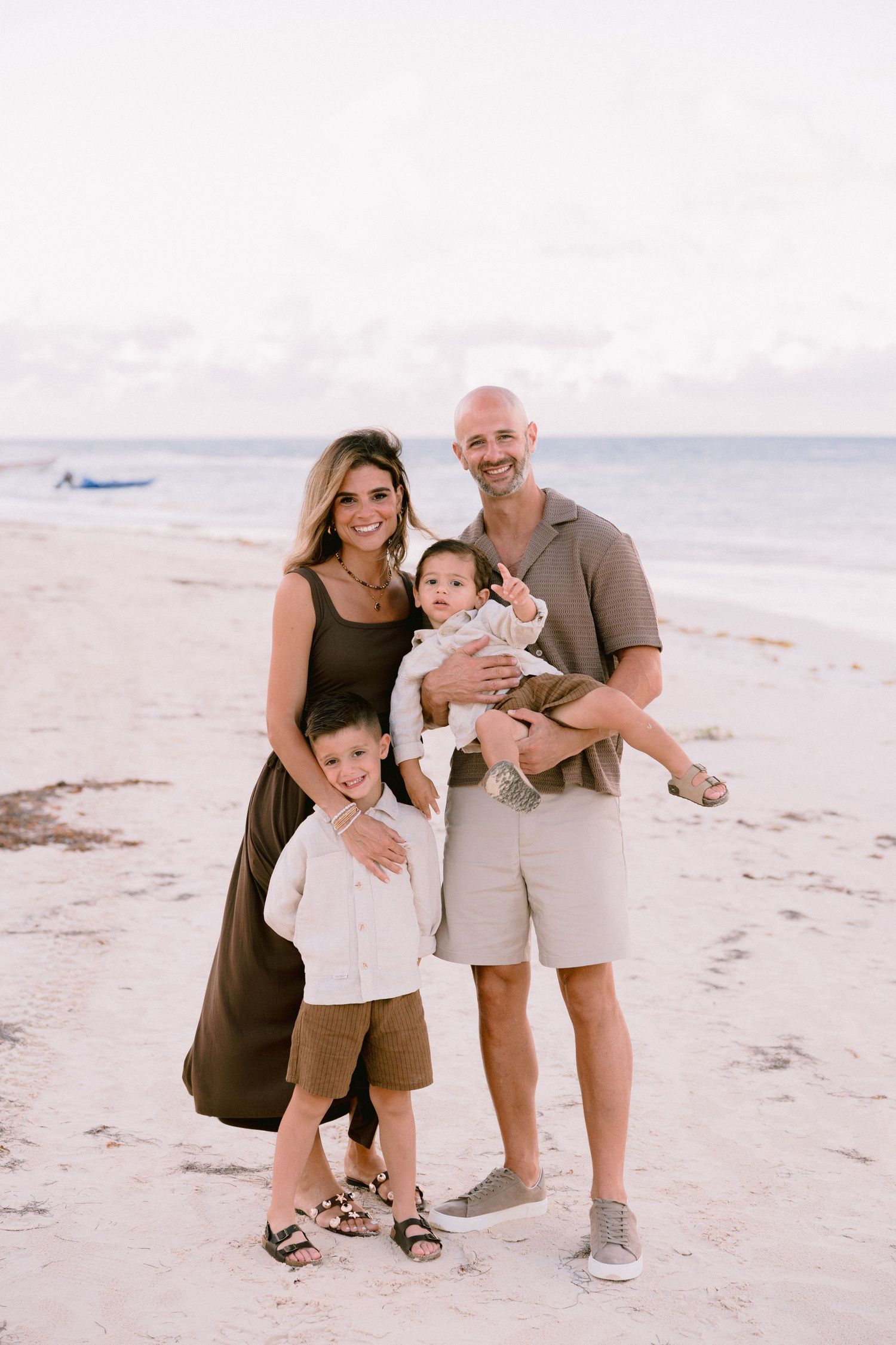 A family shares joyful moments together during a beach photoshoot in matching brown and beige outfits.