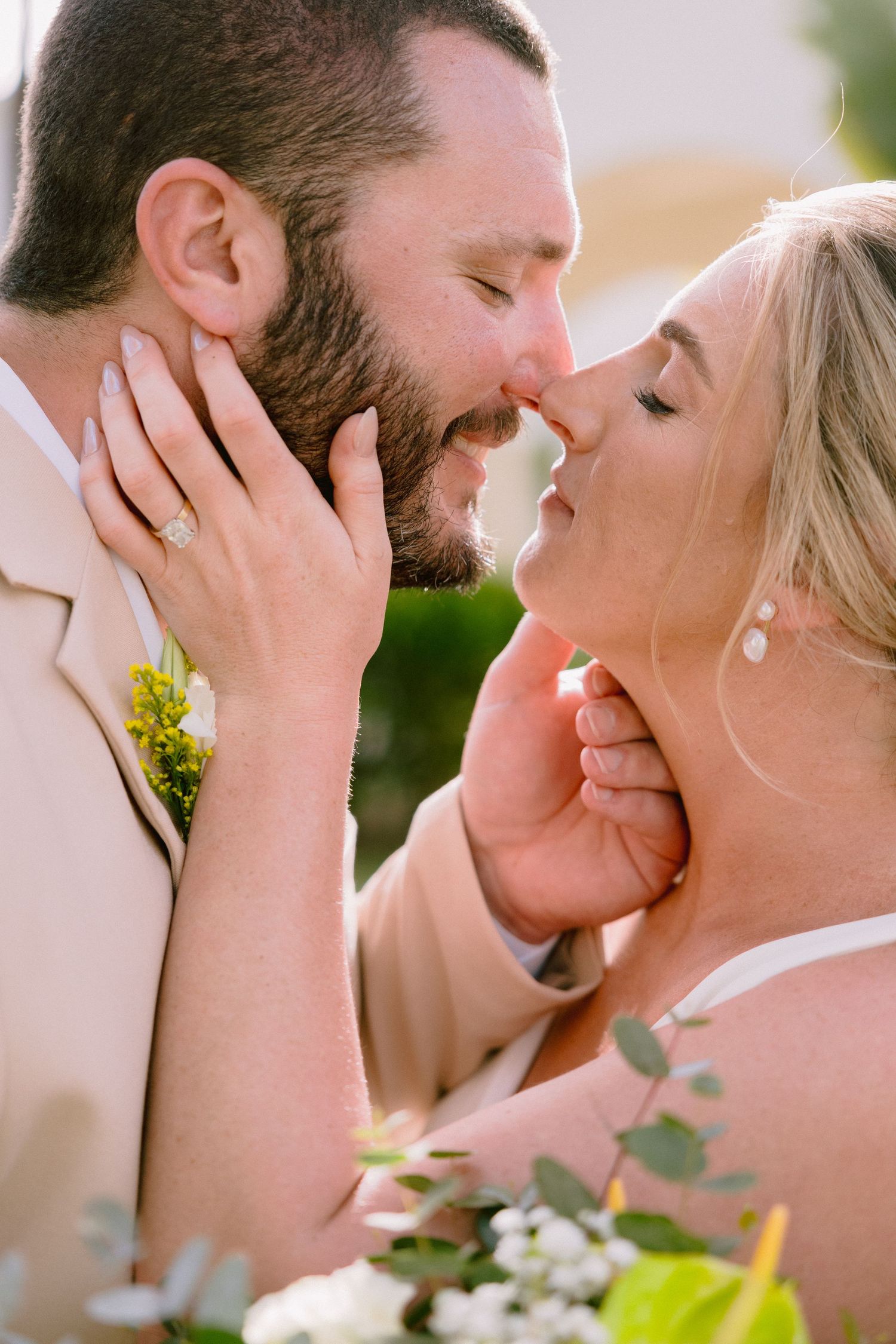 A bride and groom share a romantic almost-kiss moment, with the bride holding a white floral bouquet on their wedding day.