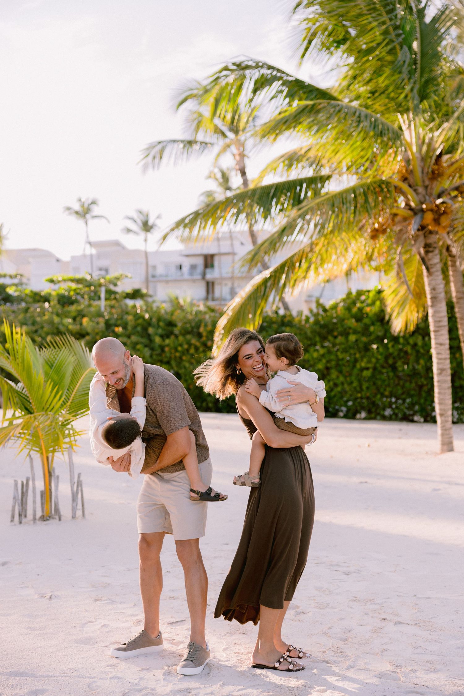 Romantic couples share intimate moments during a sunset beach photoshoot with palm trees in the background.