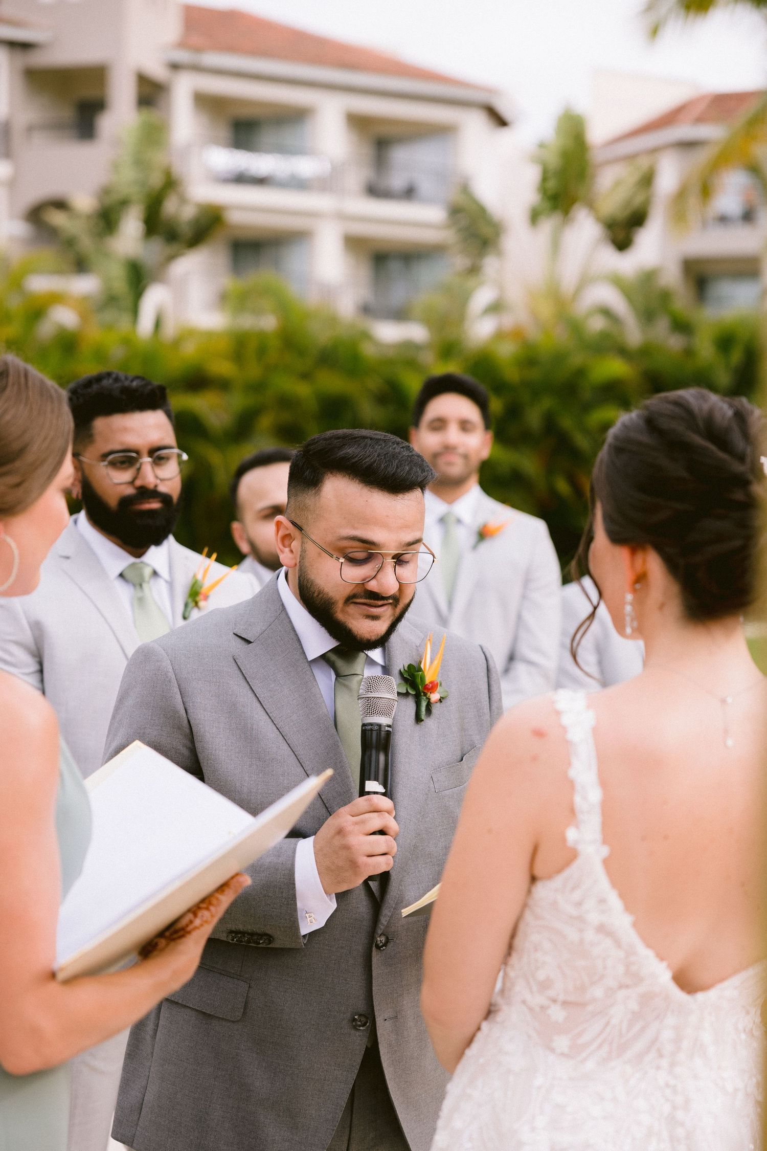 Emotional wedding ceremony moment showing groom in gray suit reacting during vows at outdoor venue.