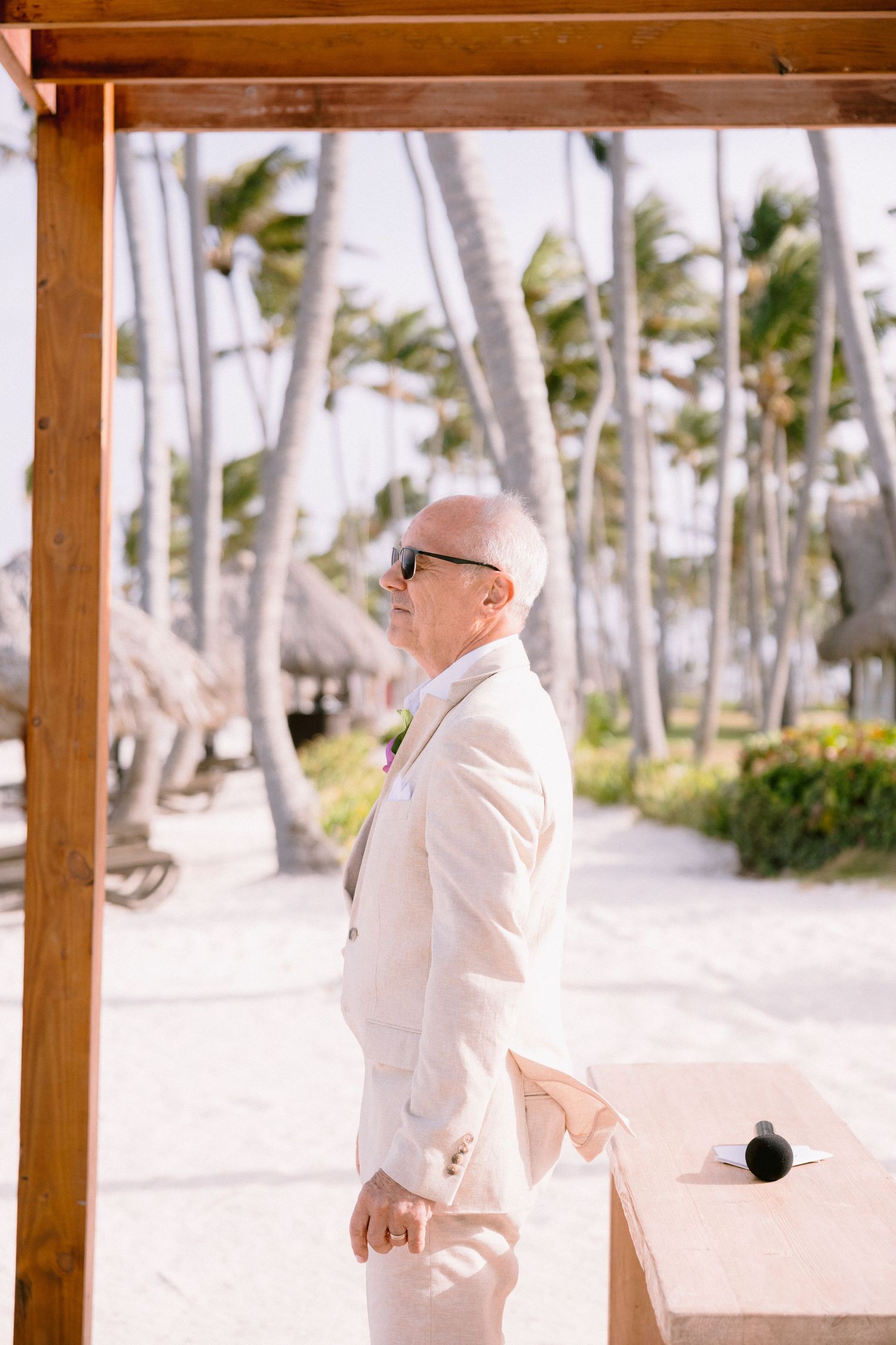 A person in white clothing walks along a tropical beach path lined with tall palm trees on a sunny day.