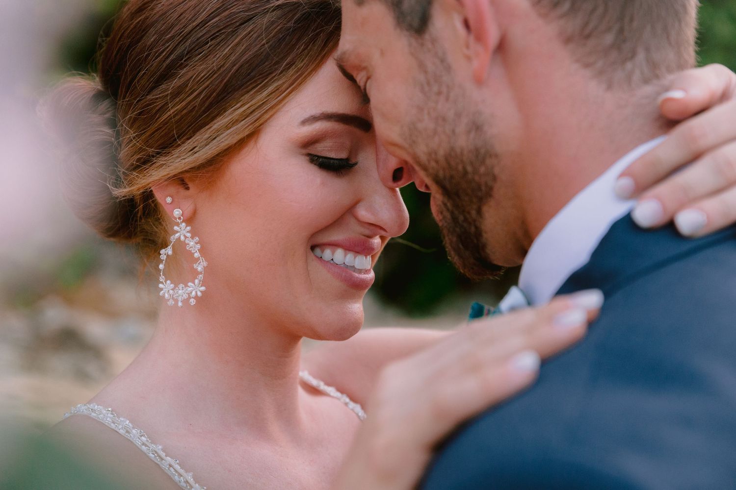 Bride and groom sharing a romantic forehead touch, smiling closely, bride wearing crystal drop earrings and wedding gown.