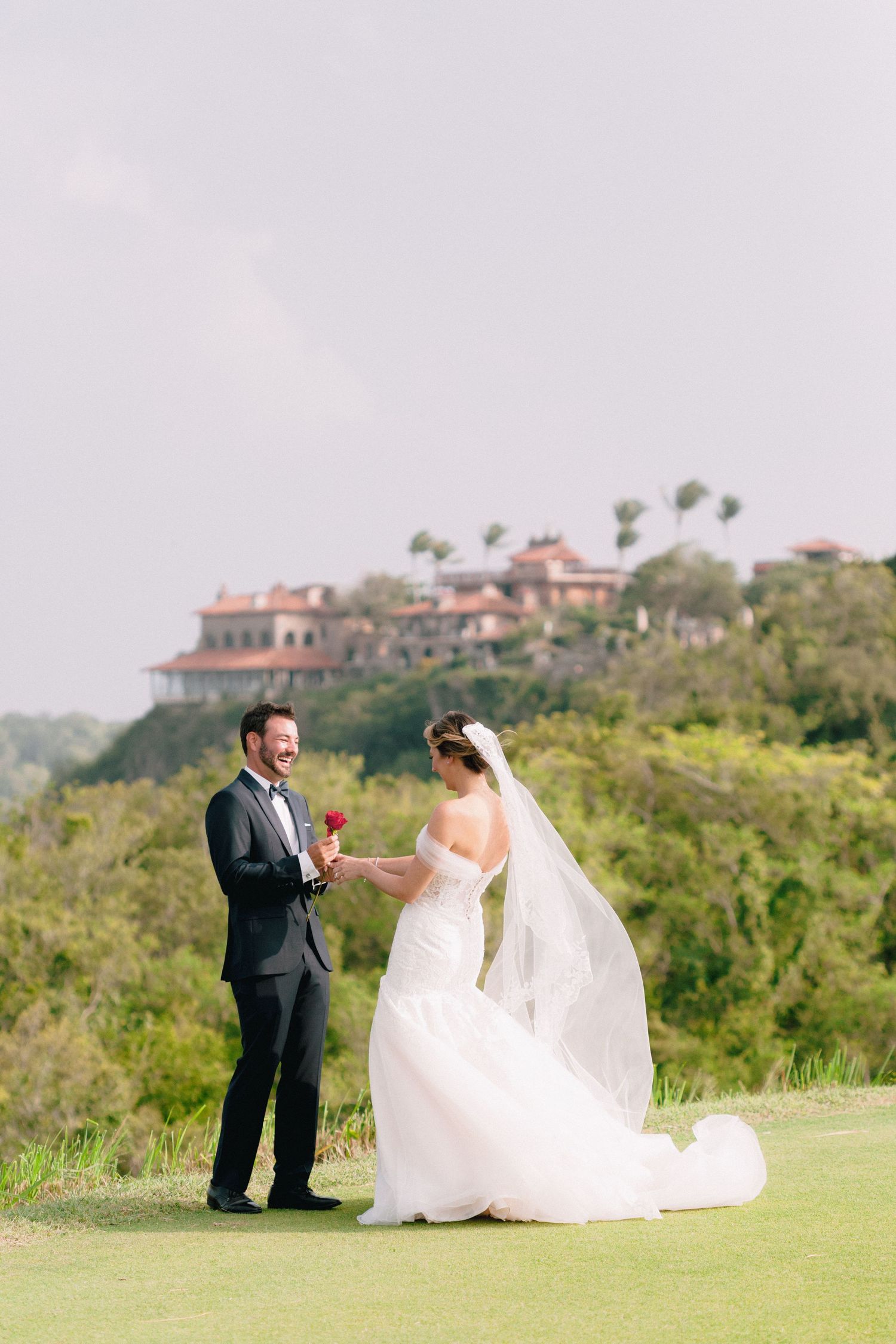 Bride and groom share a romantic moment on a golf course with a scenic estate in the background.