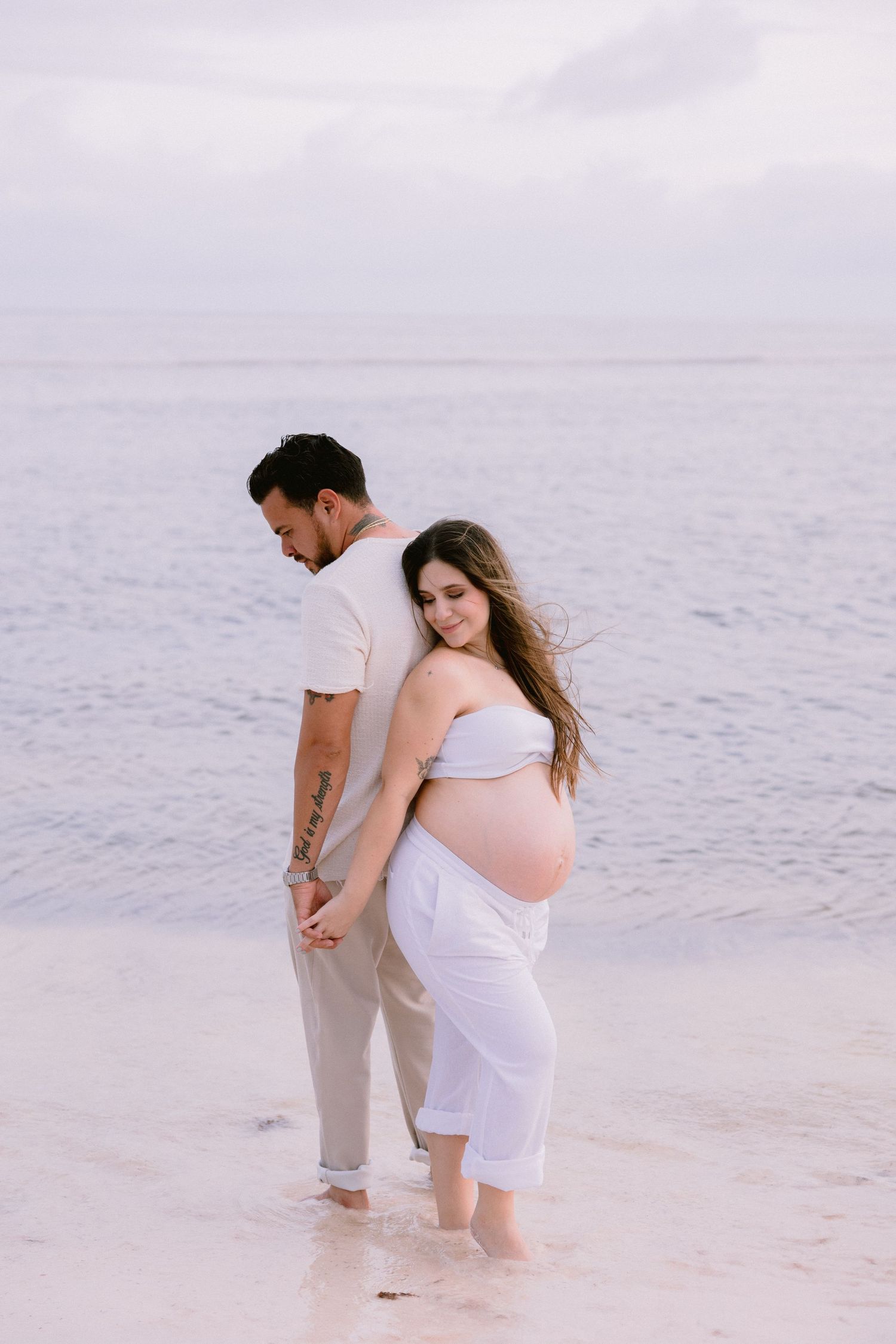 Couple in white clothing walking together along misty beach shore.
