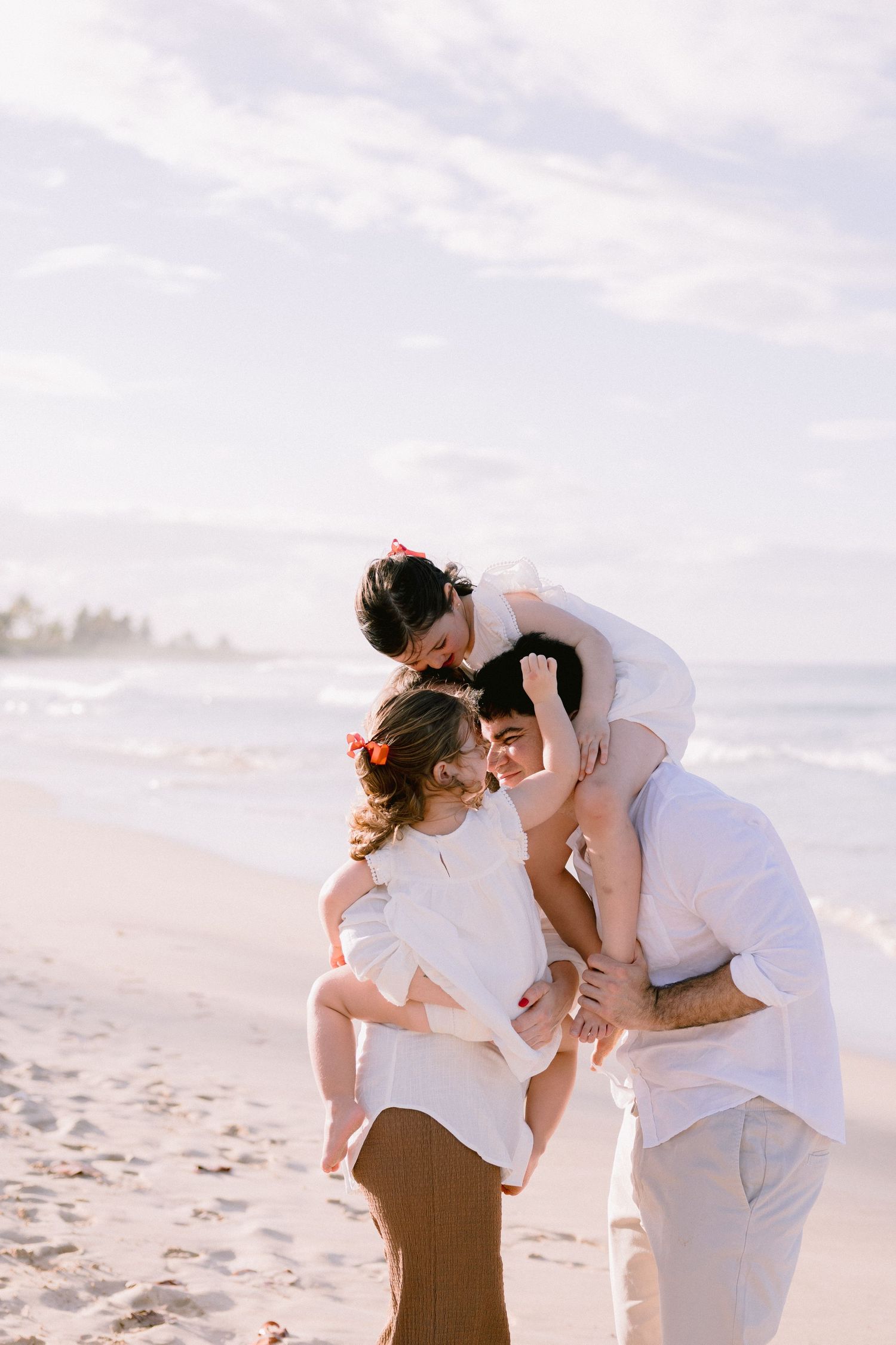 A romantic couple embraces and kisses on a sunlit beach with soft white sand and ocean waves in the background.