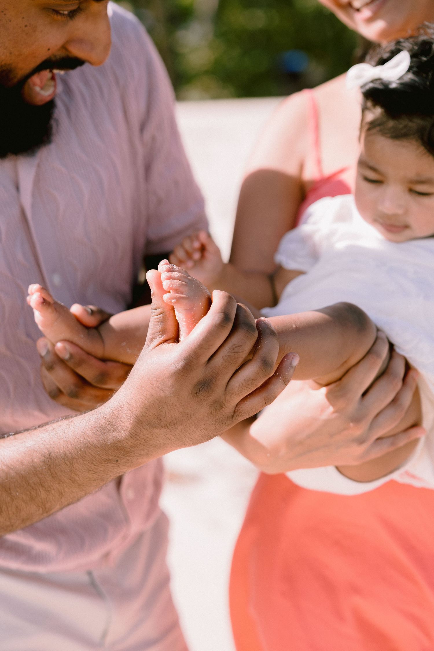 A family tenderly holds a baby's feet outdoors in warm sunlight, sharing a joyful moment together.