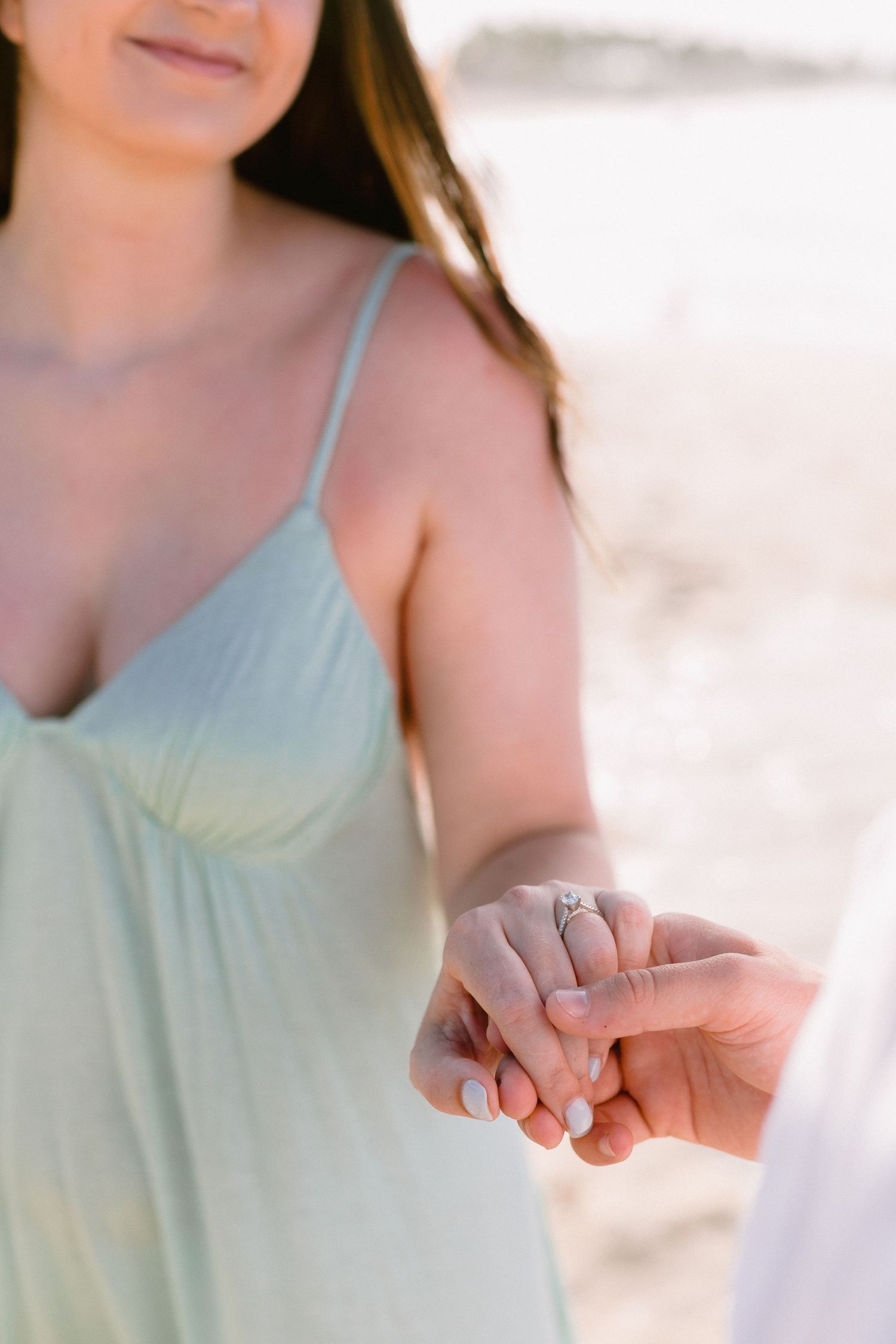 Close-up view of hands showing a diamond engagement ring on the beach.