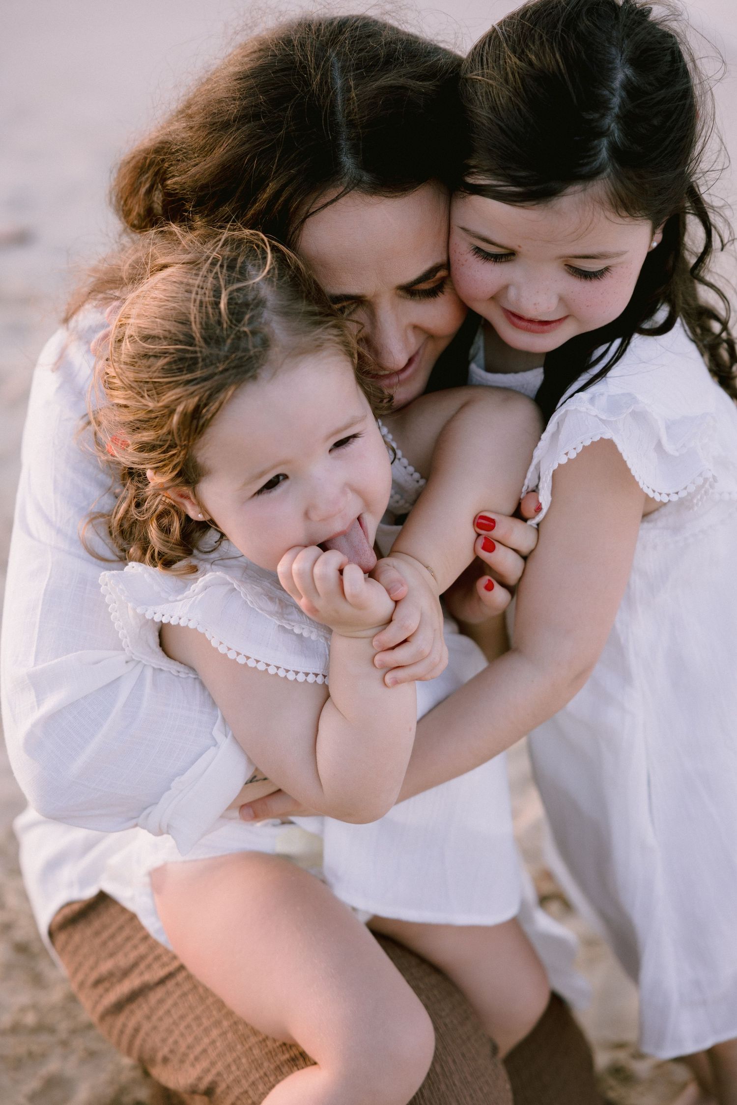 A tender moment between two people in white clothing embracing and sharing affectionate gestures on a light background.