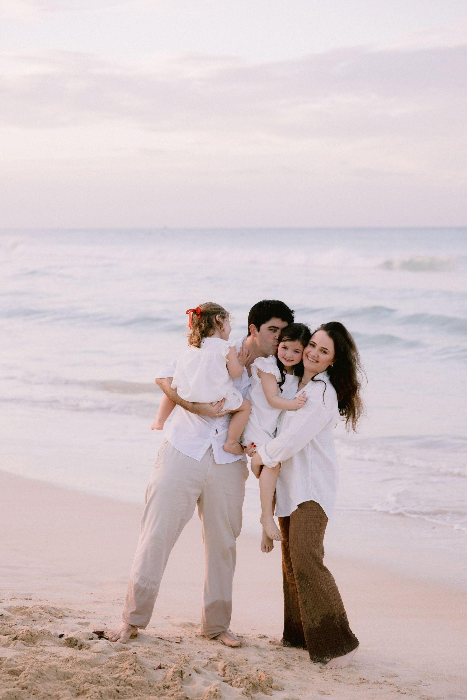 A family shares a tender moment together while standing on a peaceful beach at sunset.