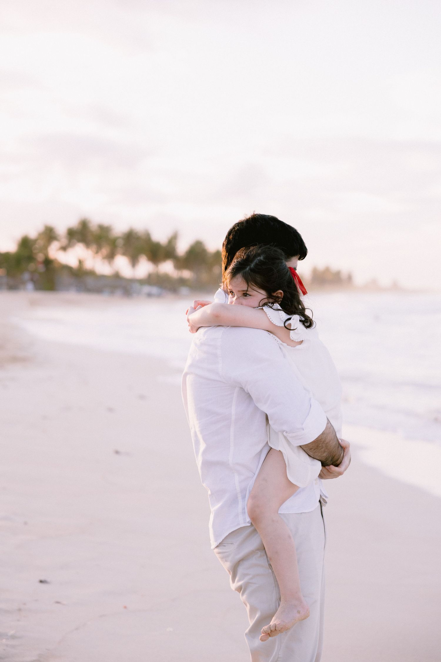 A couple in white clothing embraces on a serene beach at sunset in a series of romantic photos.
