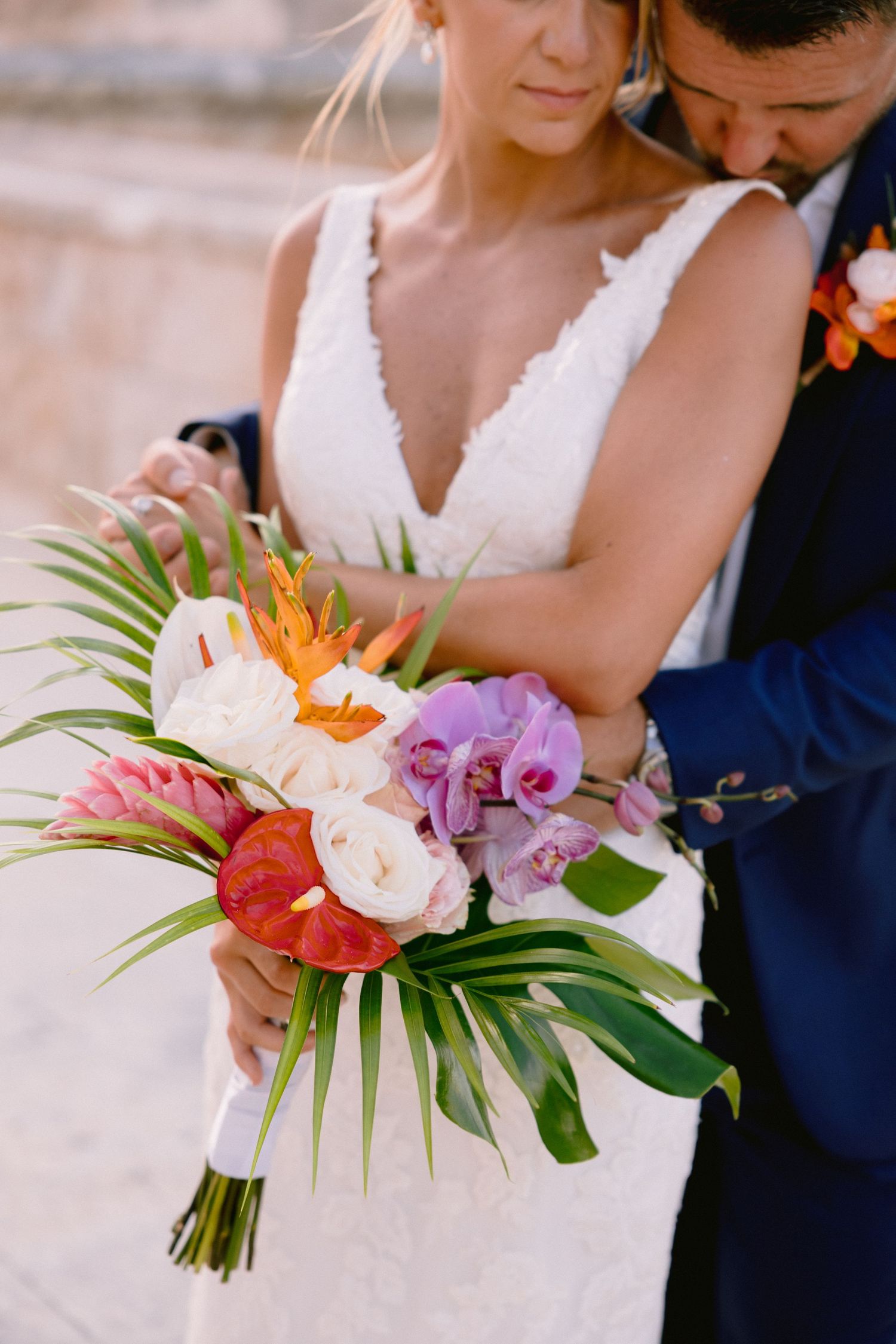 Vibrant tropical wedding bouquet with peonies, orchids, and palm fronds arranged with bright orange flowers and greenery.