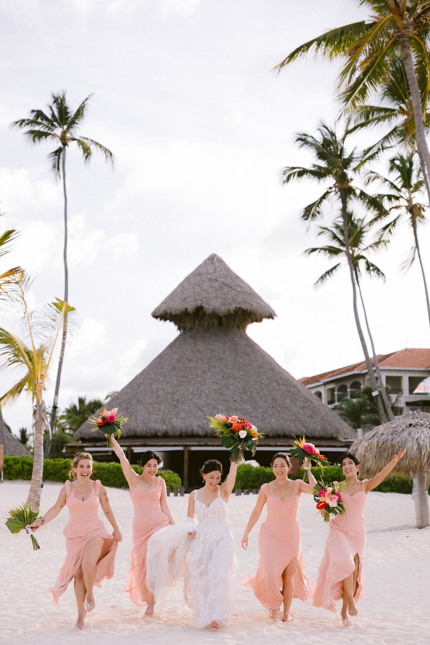 Group celebrating on a tropical beach with palm trees and thatched-roof palapa in the background.
