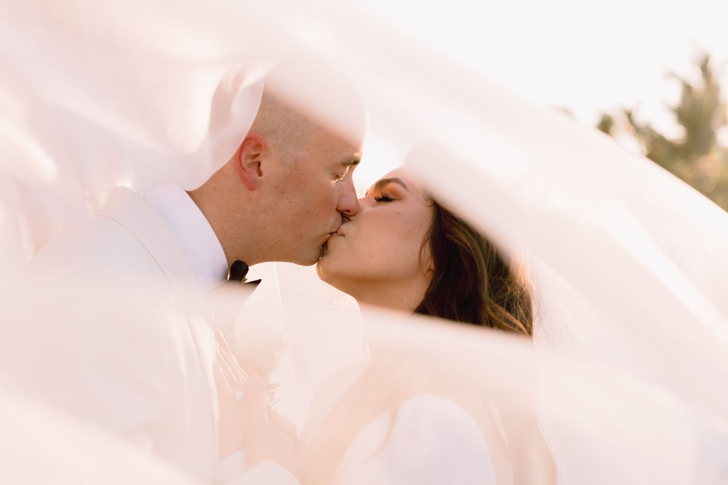 A couple shares a tender kiss during their wedding ceremony with soft pink lighting and romantic atmosphere.