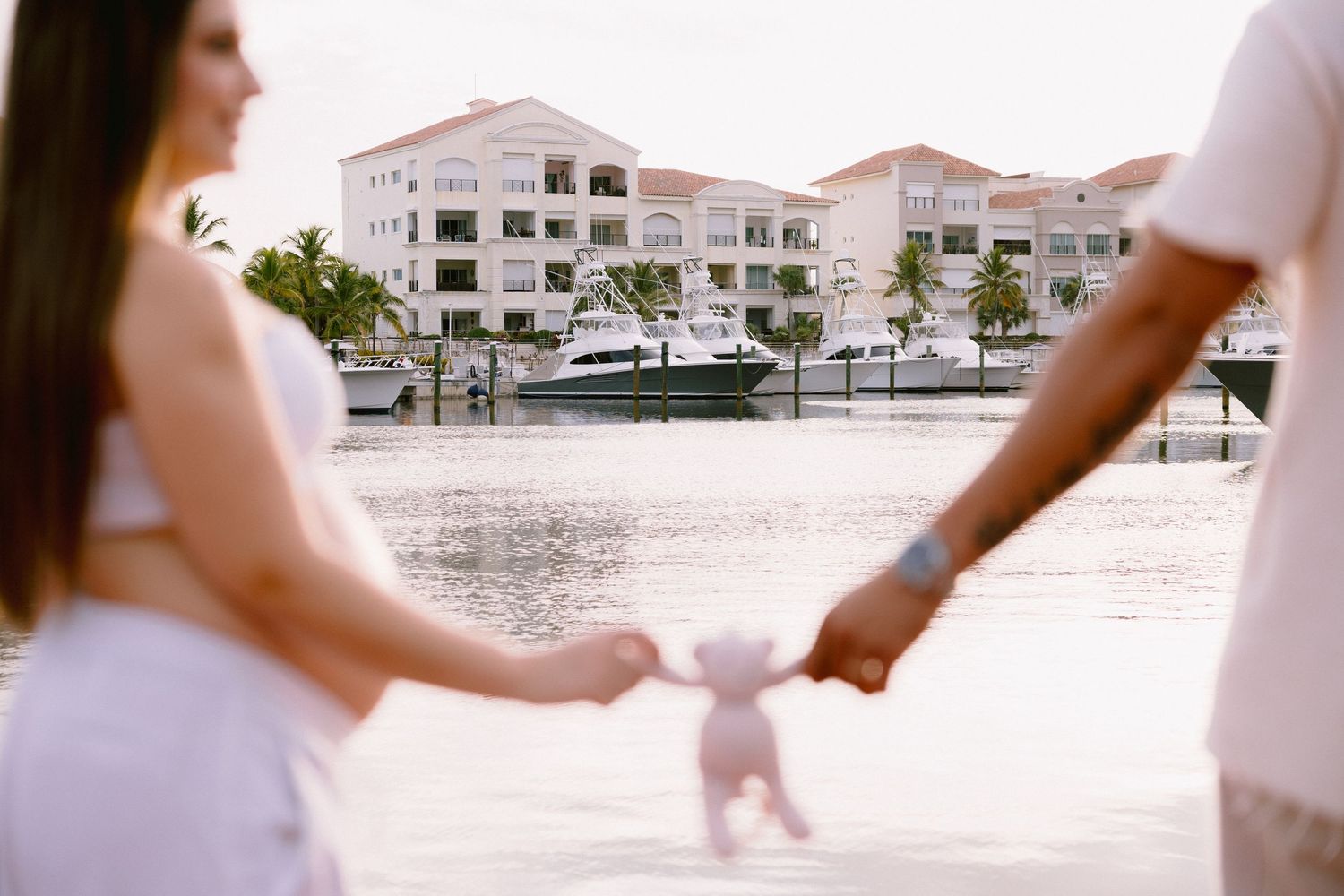 Two pairs of hands hold a small bowl in front of a beige and white building with palm trees.