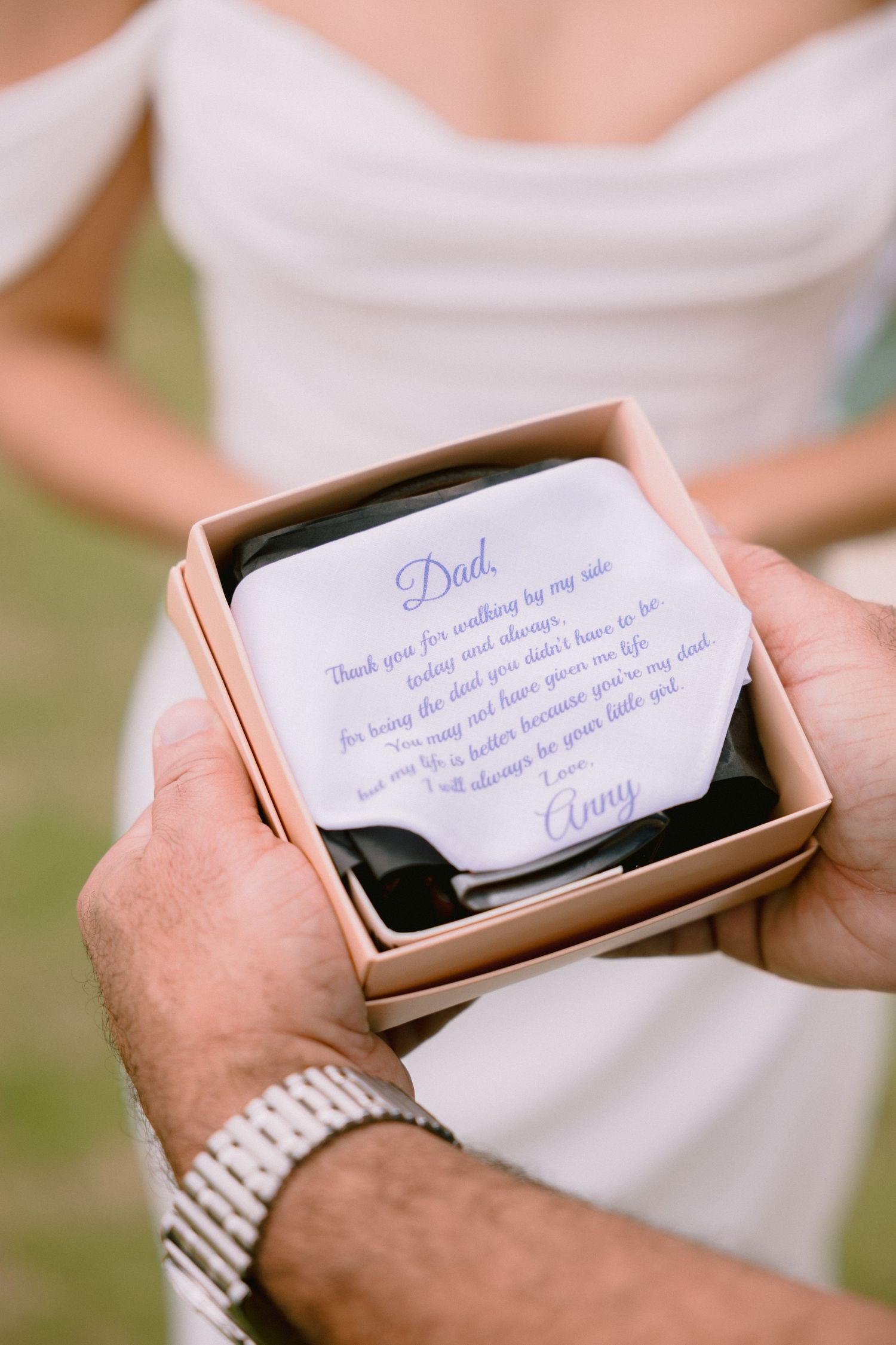 Bride presenting father with personalized wedding handkerchief in gift box, reading heartfelt message signed by daughter Anny.