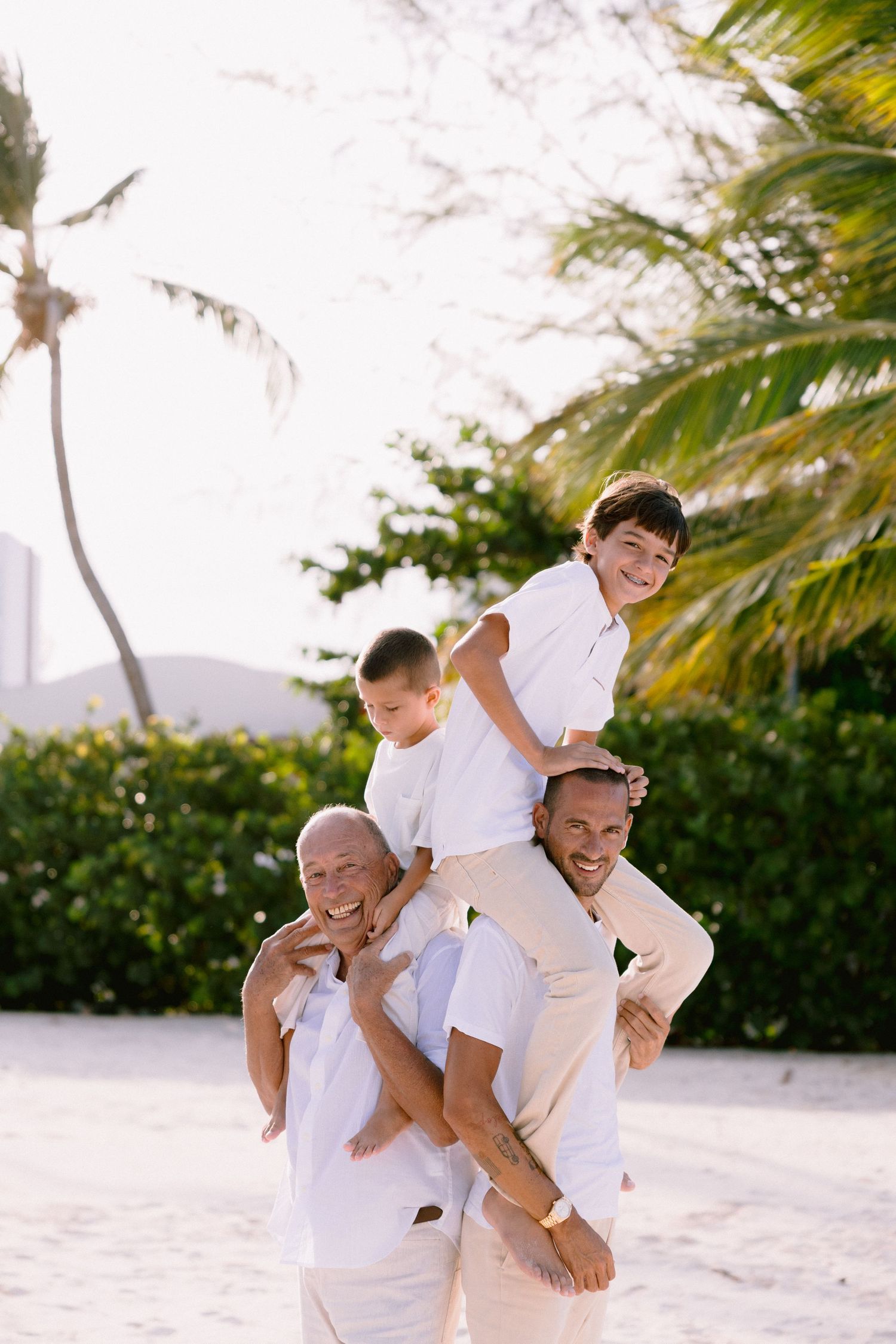 Family enjoying a playful moment together on a tropical beach with palm trees in the background.