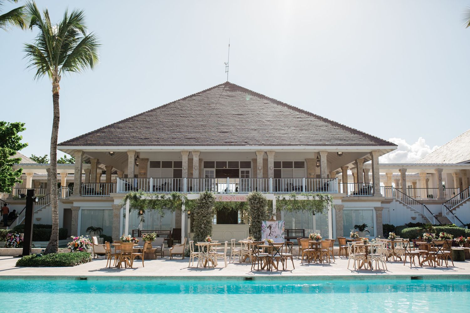Elegant poolside pavilion with palm tree at luxury resort featuring white columns and outdoor dining furniture.