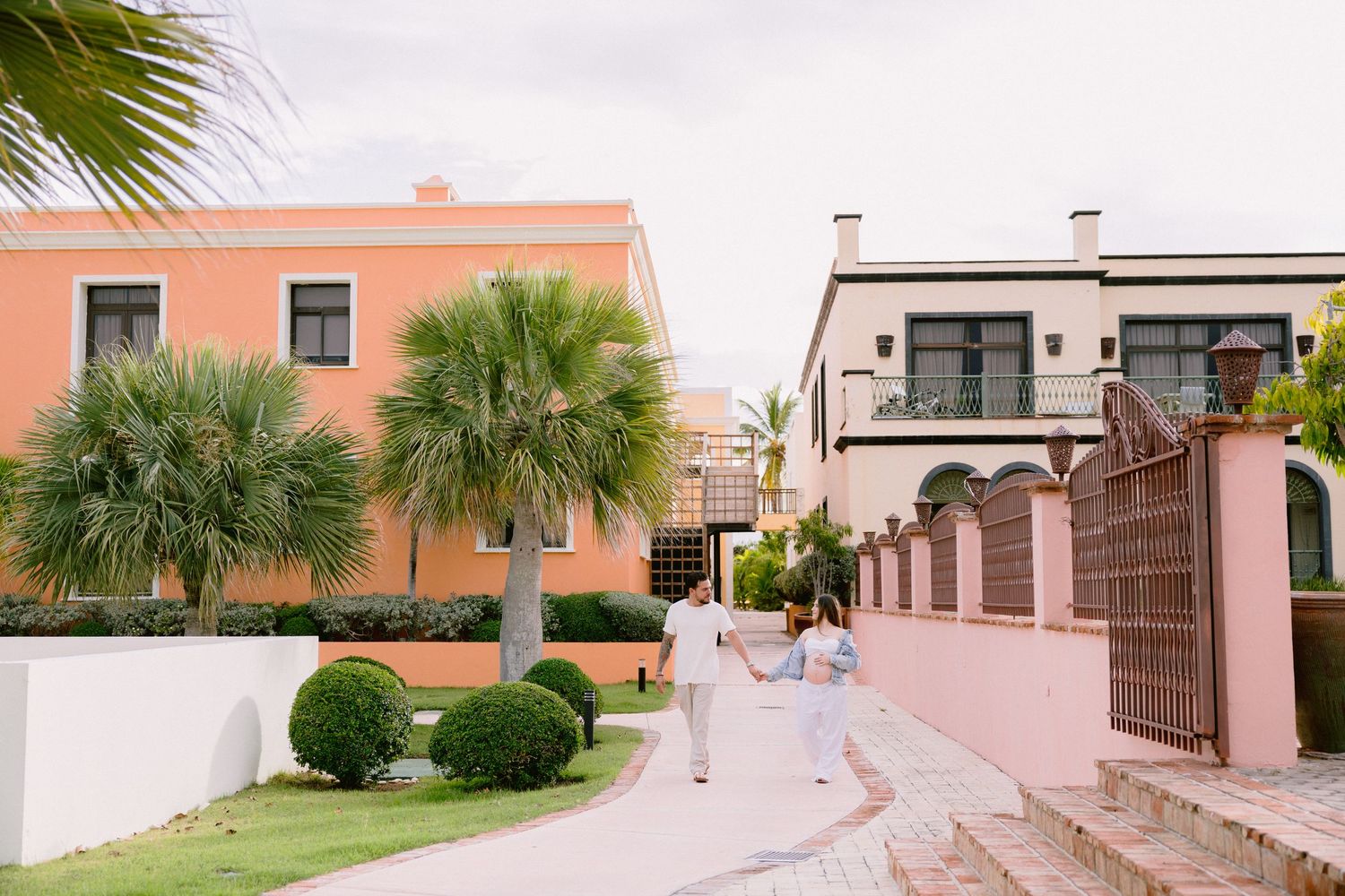 Panoramic view of a tropical beachfront resort with palm trees and peach-colored buildings under sunny skies.
