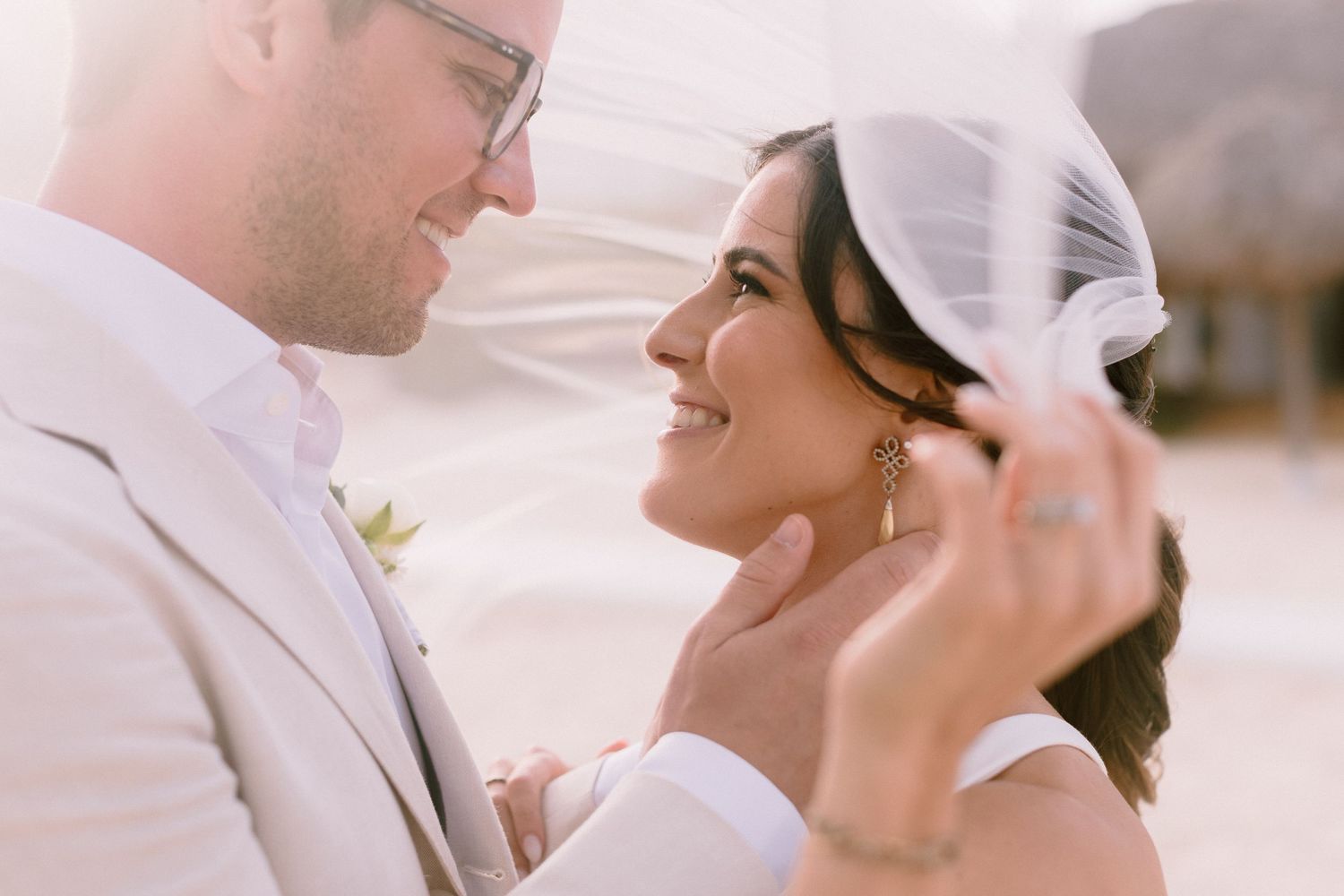 Bride and groom share a romantic moment under a flowing veil on their wedding day.
