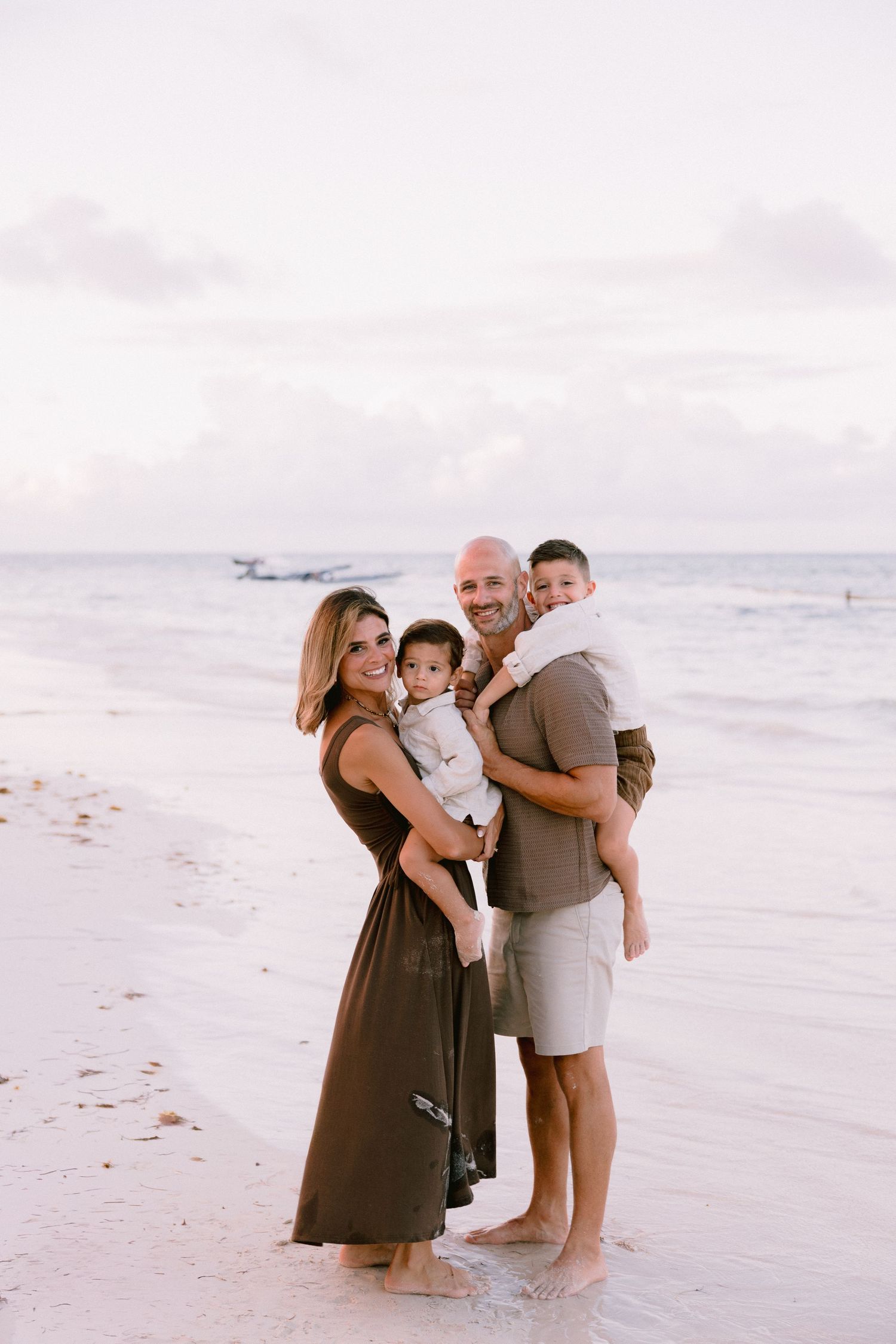 A family shares tender moments together while standing on a peaceful beach at sunset.