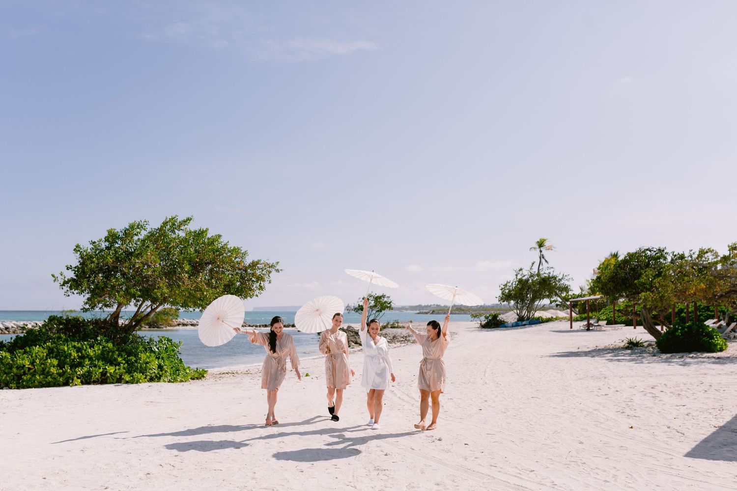 People walking along a pristine white sand beach with turquoise waters and tropical vegetation in the background.
