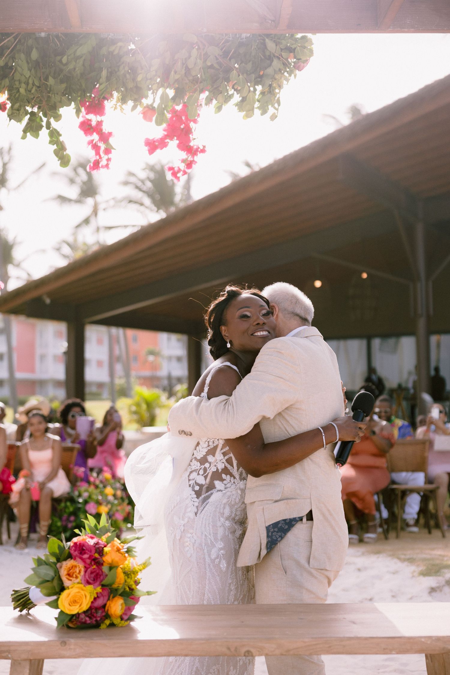 A joyful couple shares a romantic kiss during their outdoor wedding reception celebration with colorful flowers nearby.