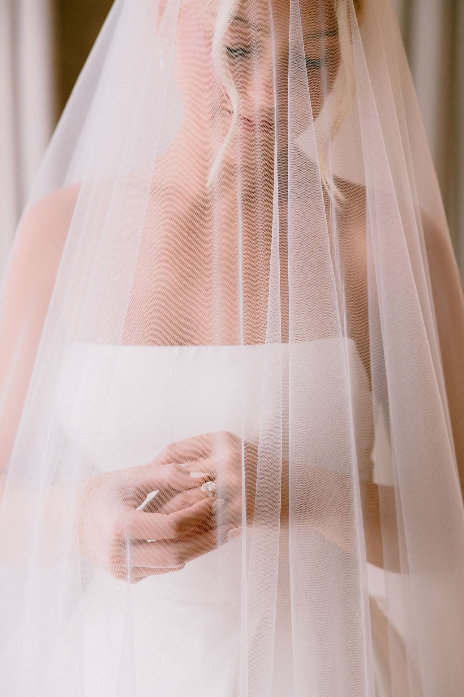 Bride in strapless white gown and sheer veil looking down at her diamond engagement ring.
