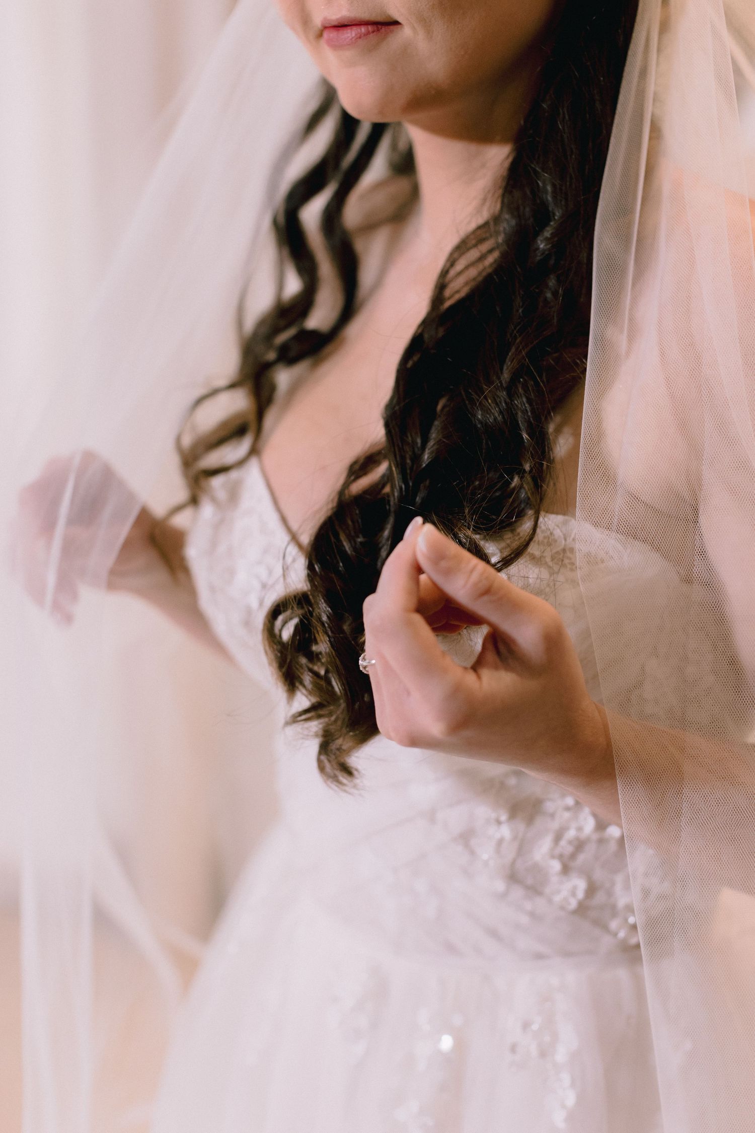 Bride in white lace wedding dress and veil with dark curly hair, delicately holding her gown before the ceremony.
