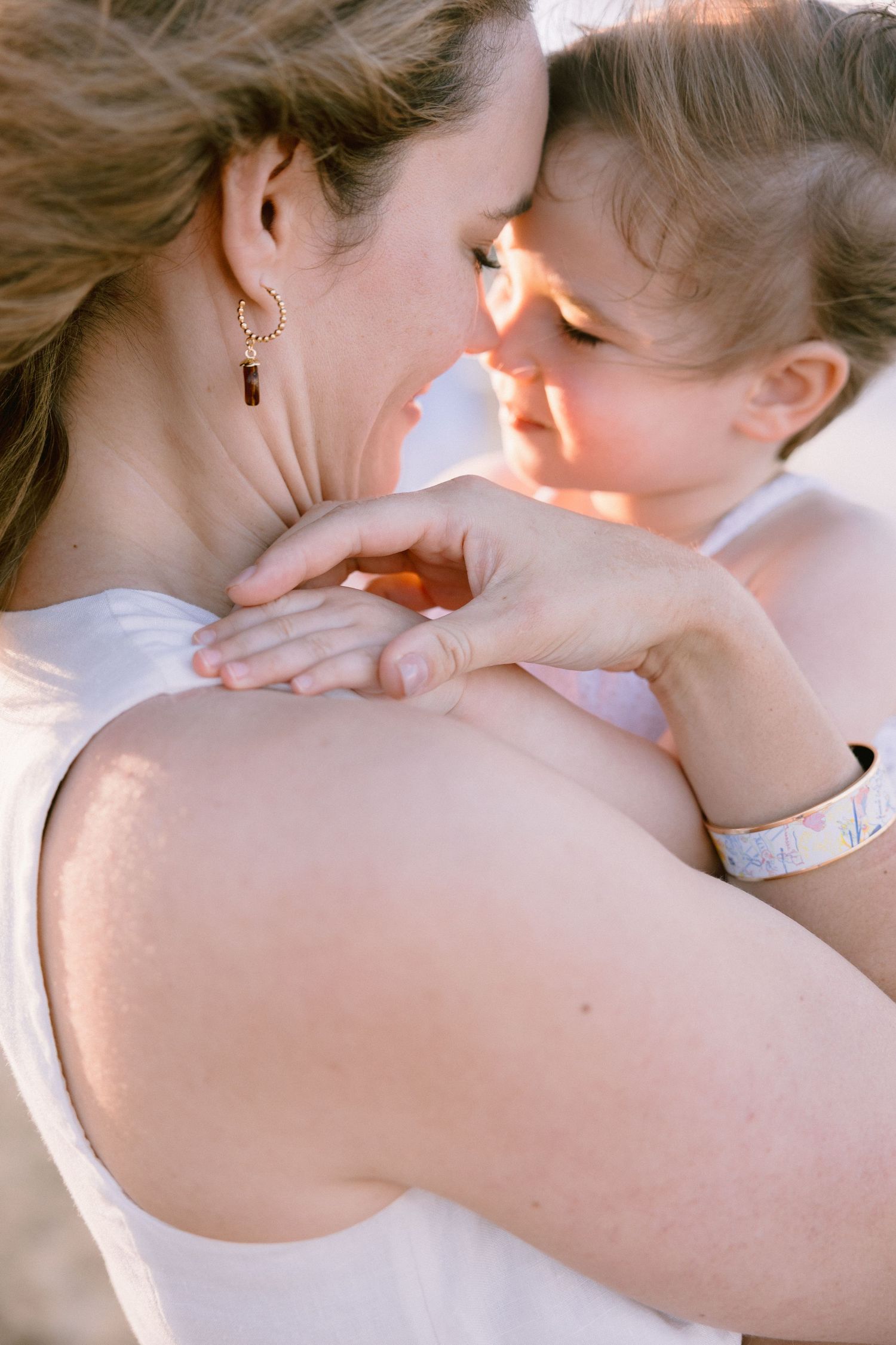 A mother tenderly holds her young child close, their faces nearly touching in a warm, sunlit embrace.