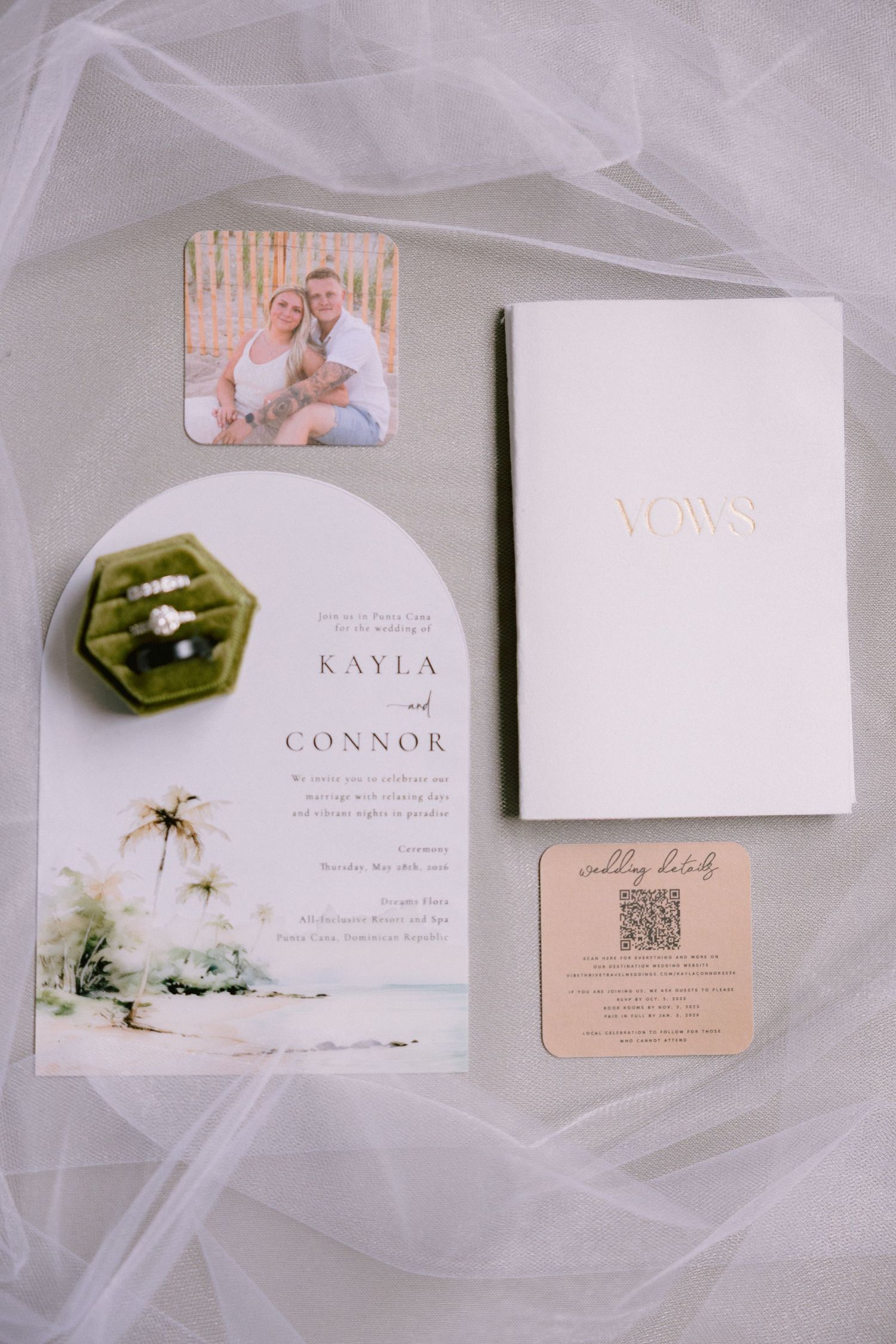 Wedding stationery flat lay featuring Kayla and Connor's invitation suite, vows book, ring box, and photo on sheer fabric.