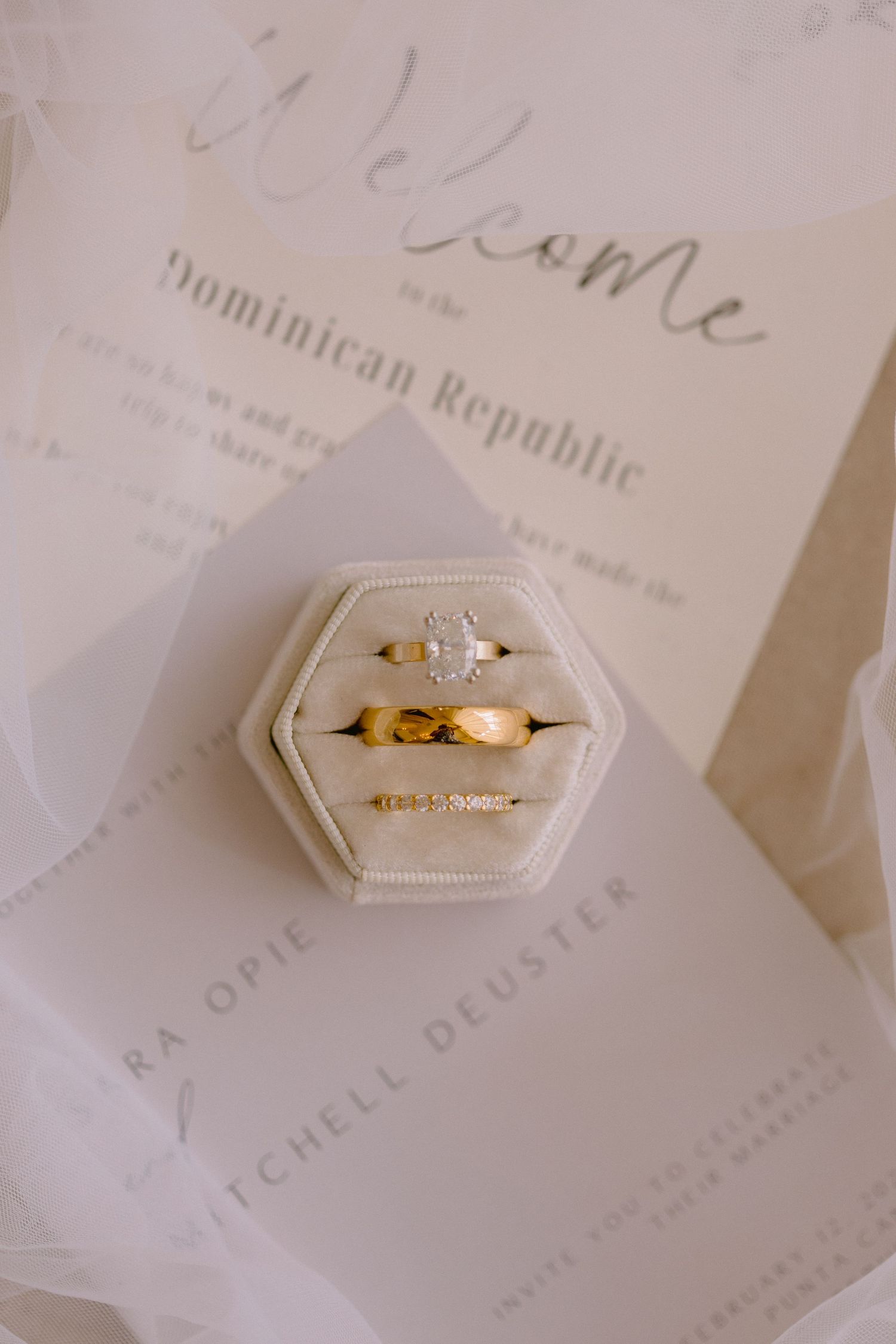 Gold wedding bands and diamond engagement ring in ivory velvet hexagon box on Dominican Republic welcome stationery.