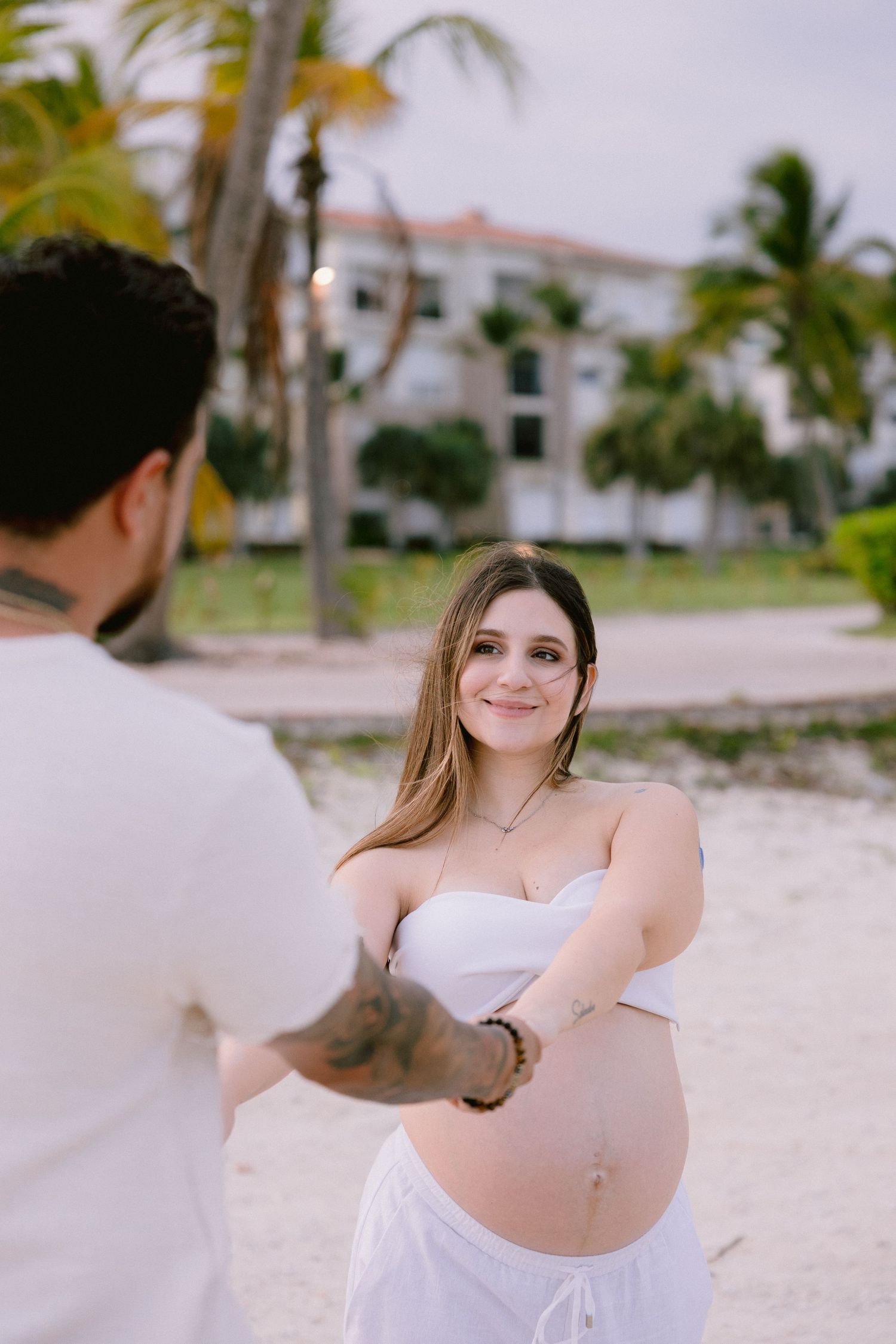 A romantic photoshoot sequence of a couple in white clothing walking along a tropical beach with palm trees.