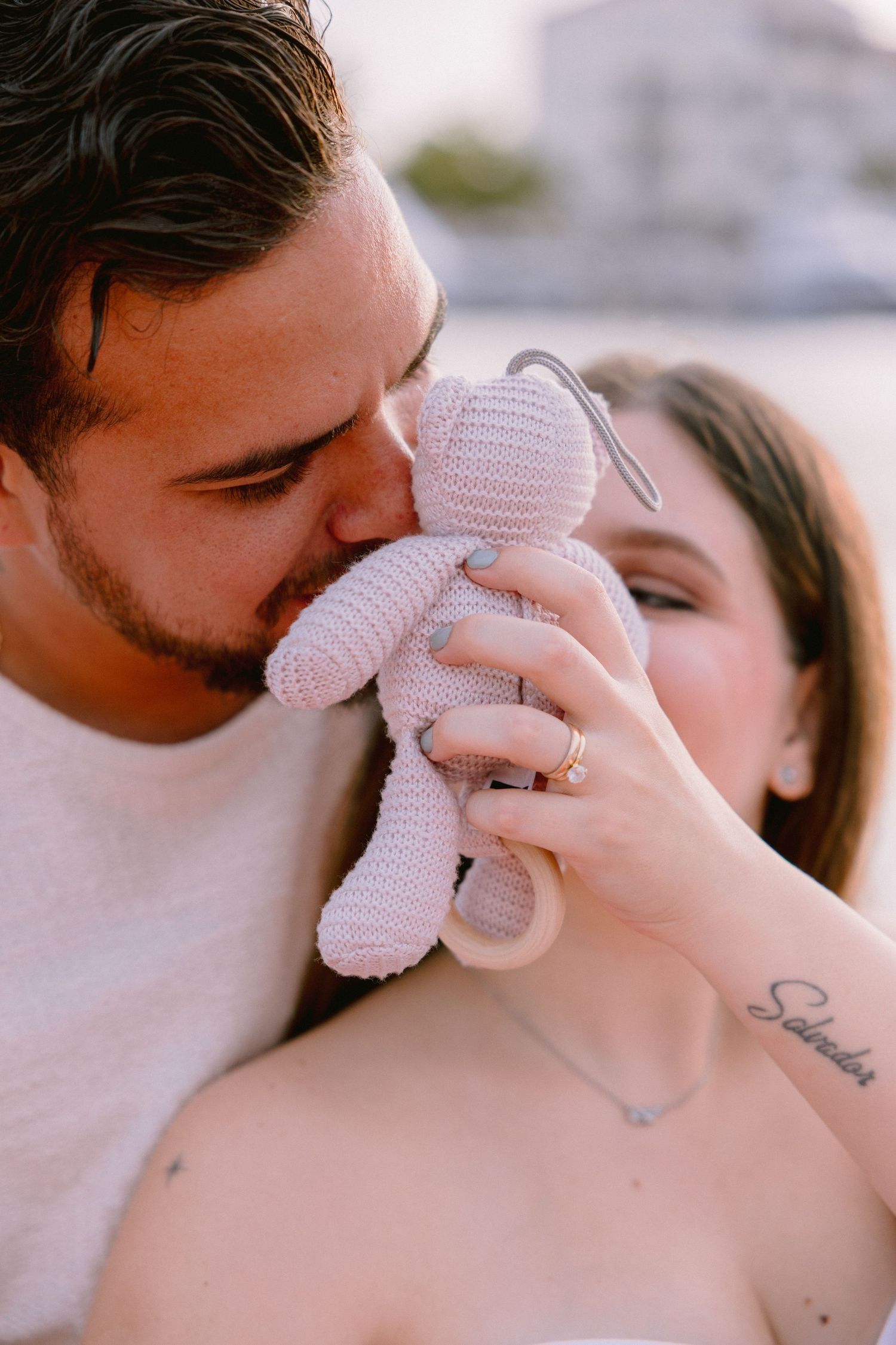 Couple shares tender moment holding small knitted stuffed toy between them during intimate portrait session.