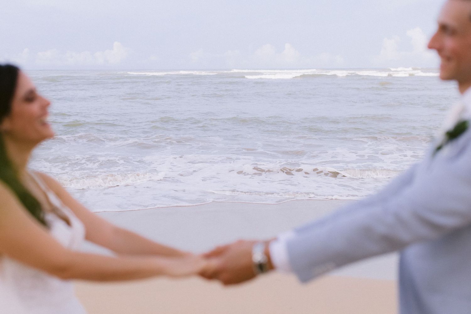 Couple holding hands and walking along the beach with ocean waves in background.