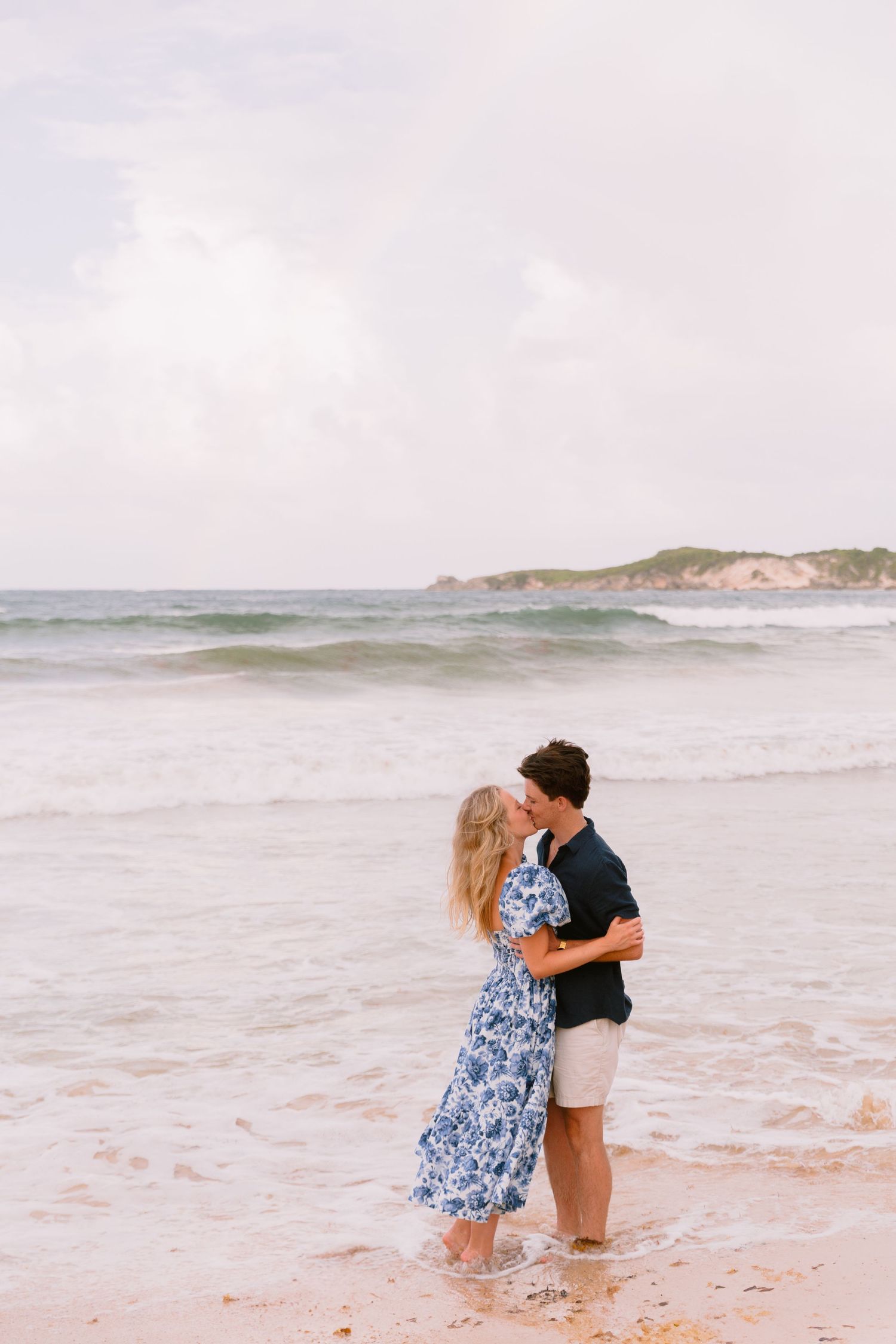 Romantic couple embracing in the ocean waves at sunset on a beach.