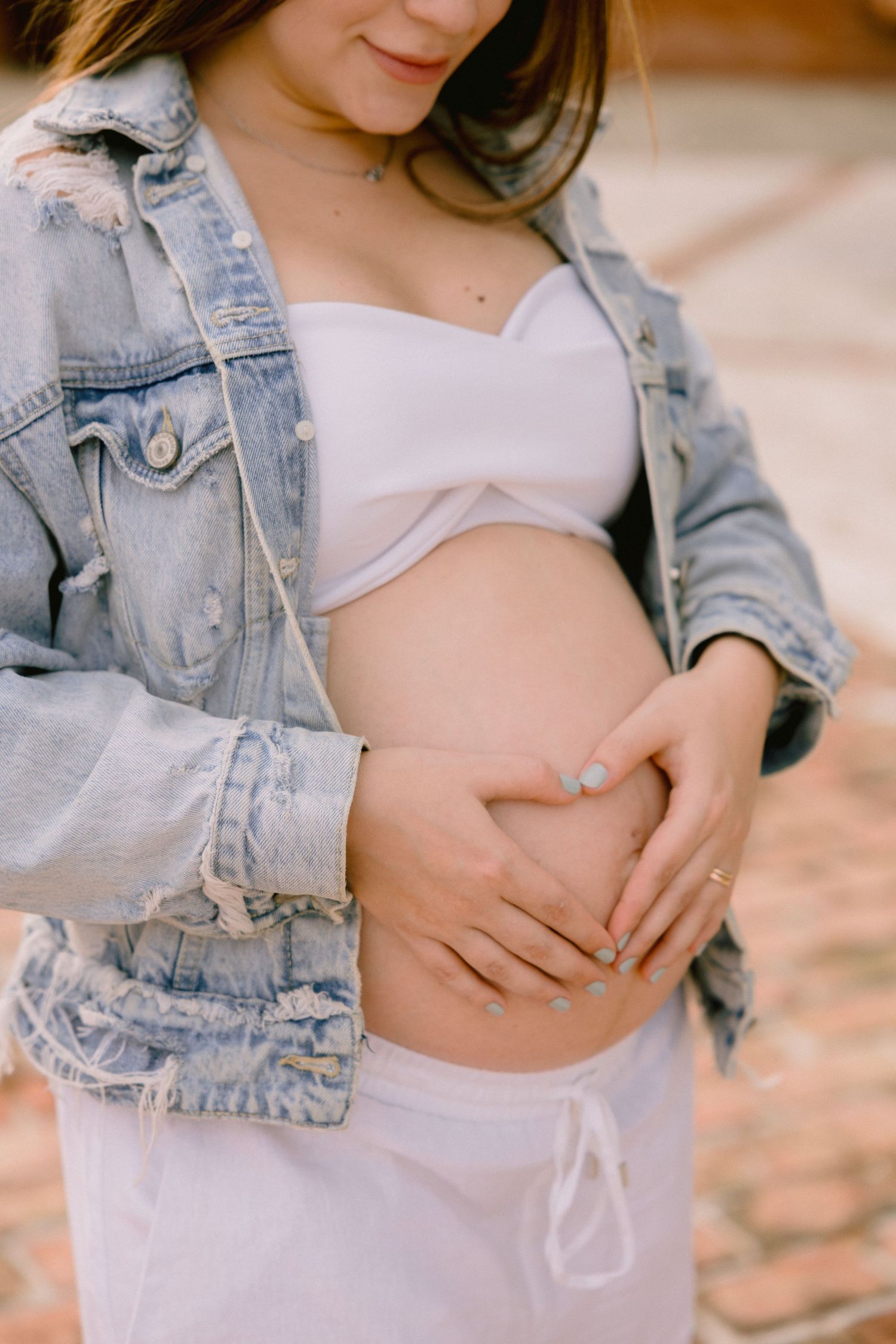 A woman in a denim jacket and light colored top poses in a maternity photo series showing her growing baby bump.