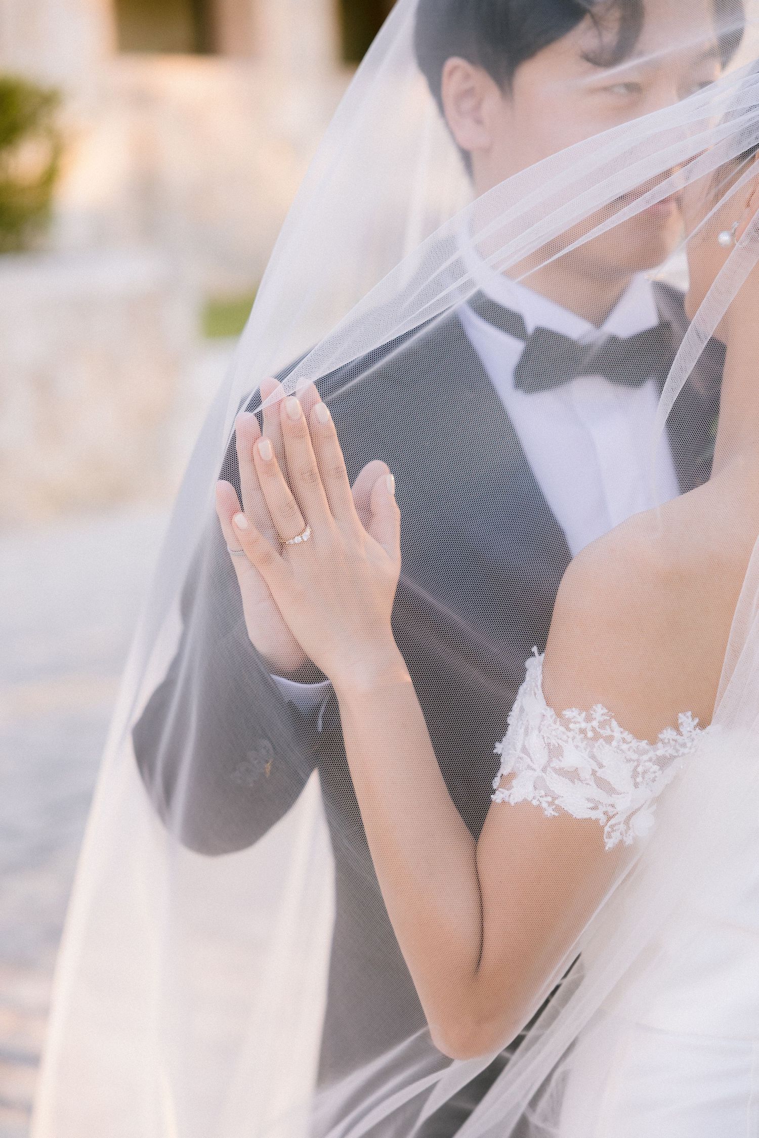 Close-up of wedding rings and lace details through delicate white veil.