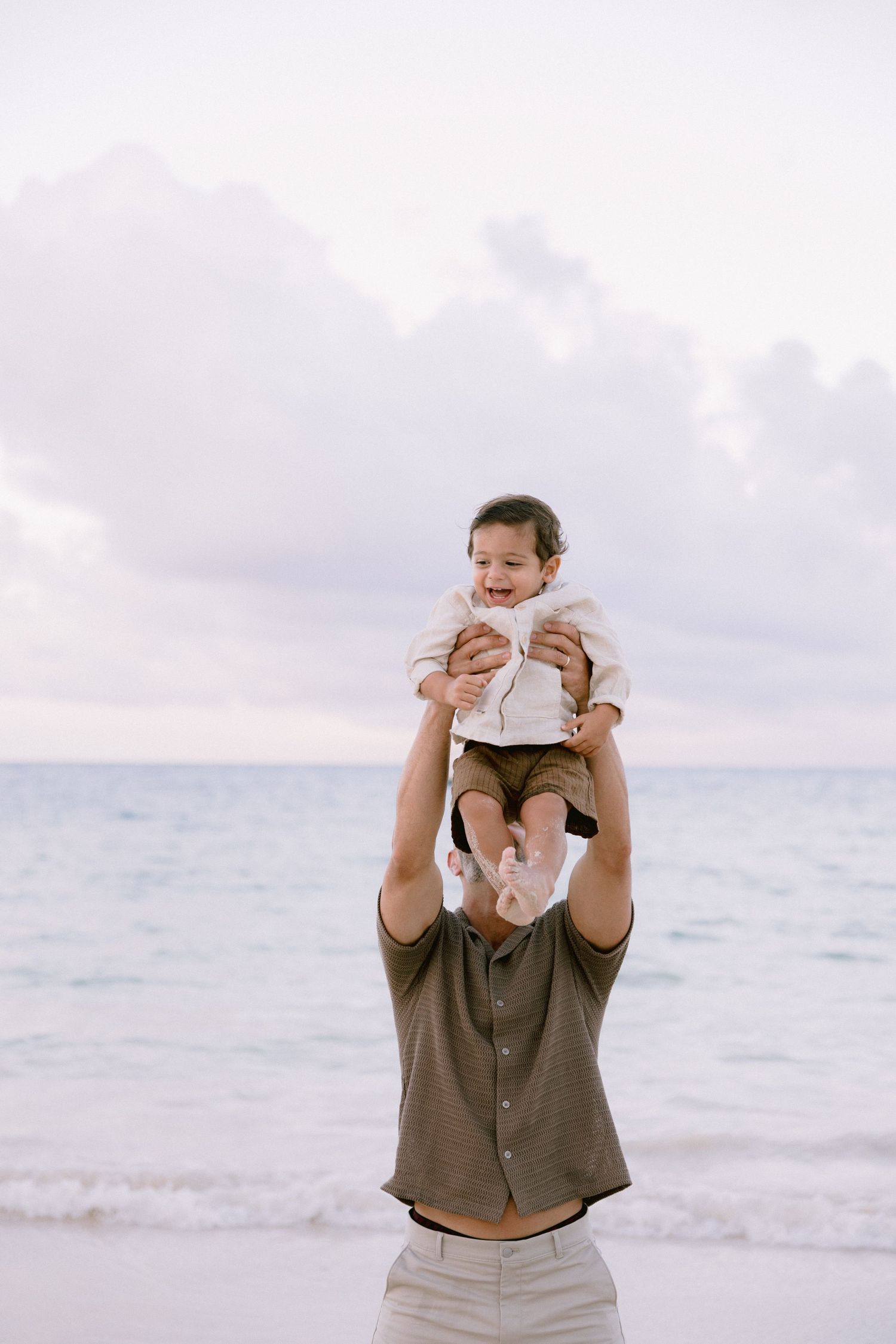 A series of four connected photos showing a person holding a baby at the beach during sunset.