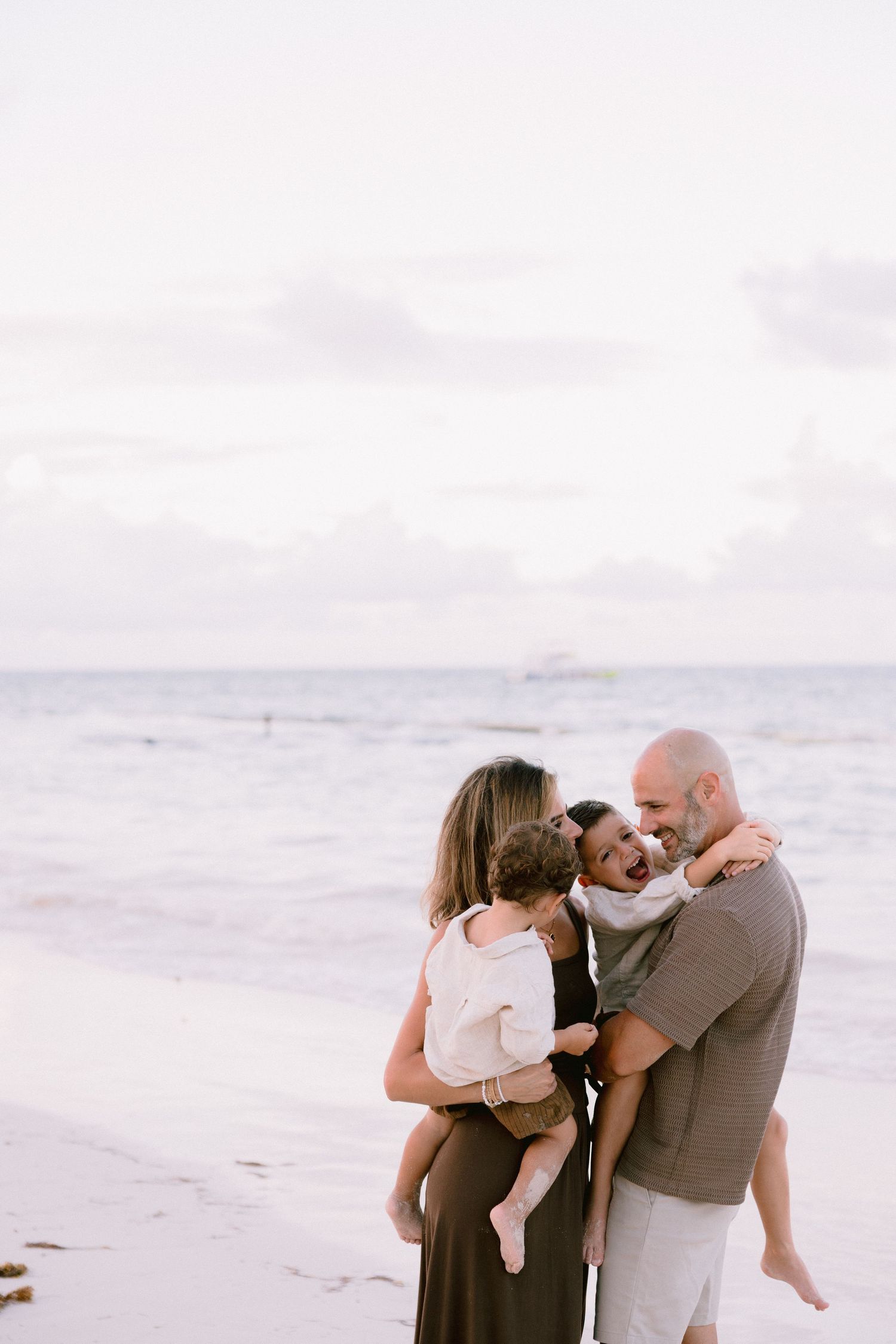 A family shares a tender moment together while standing on a serene beach at sunset.